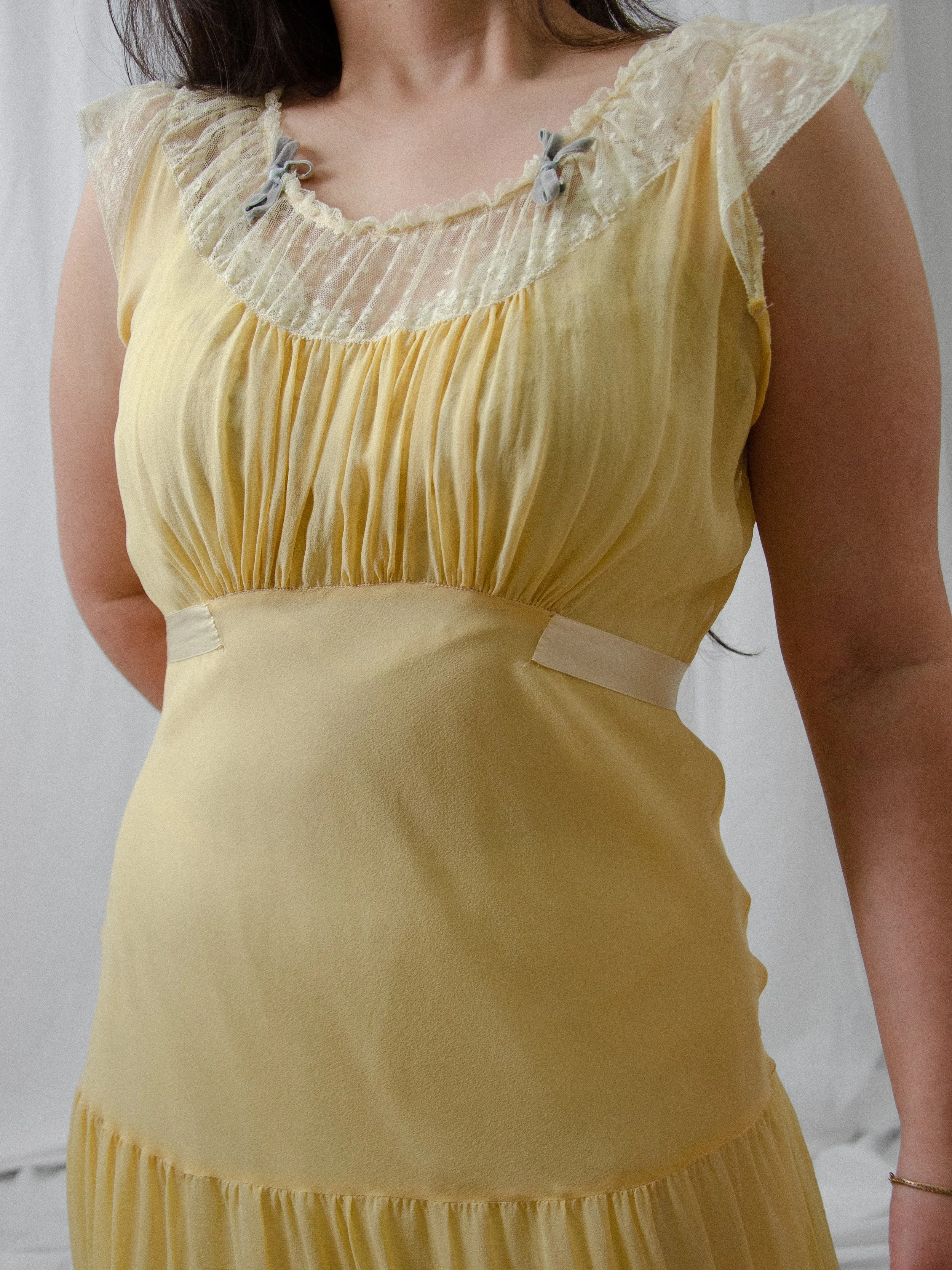 Close-up of the 1940s yellow silk dress bodice, showing the Swiss dot lace yoke and small blue velvet bows.