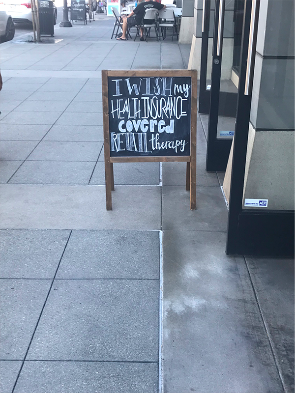 Chalk sign in front of retail store that says "I wish my health insurance covered retail therapy"