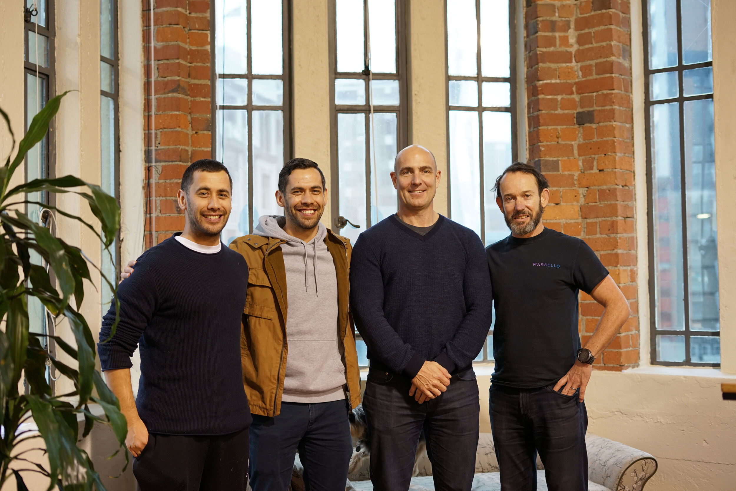 Marsello’s CEO’s stand with Goody’s CEO in front of a lead window and brick pillars. 