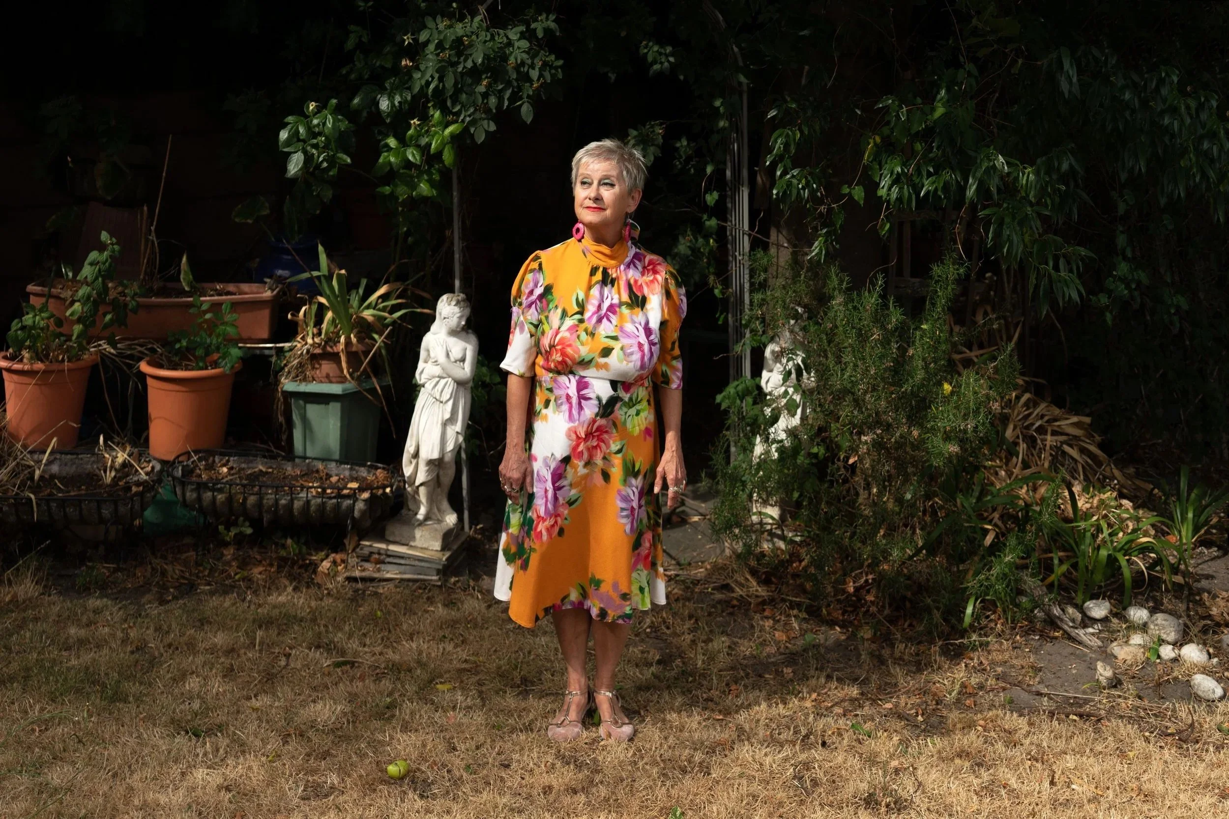 An older Polish lady wearing a brightly coloured dress photographed in a garden during a hot summer.