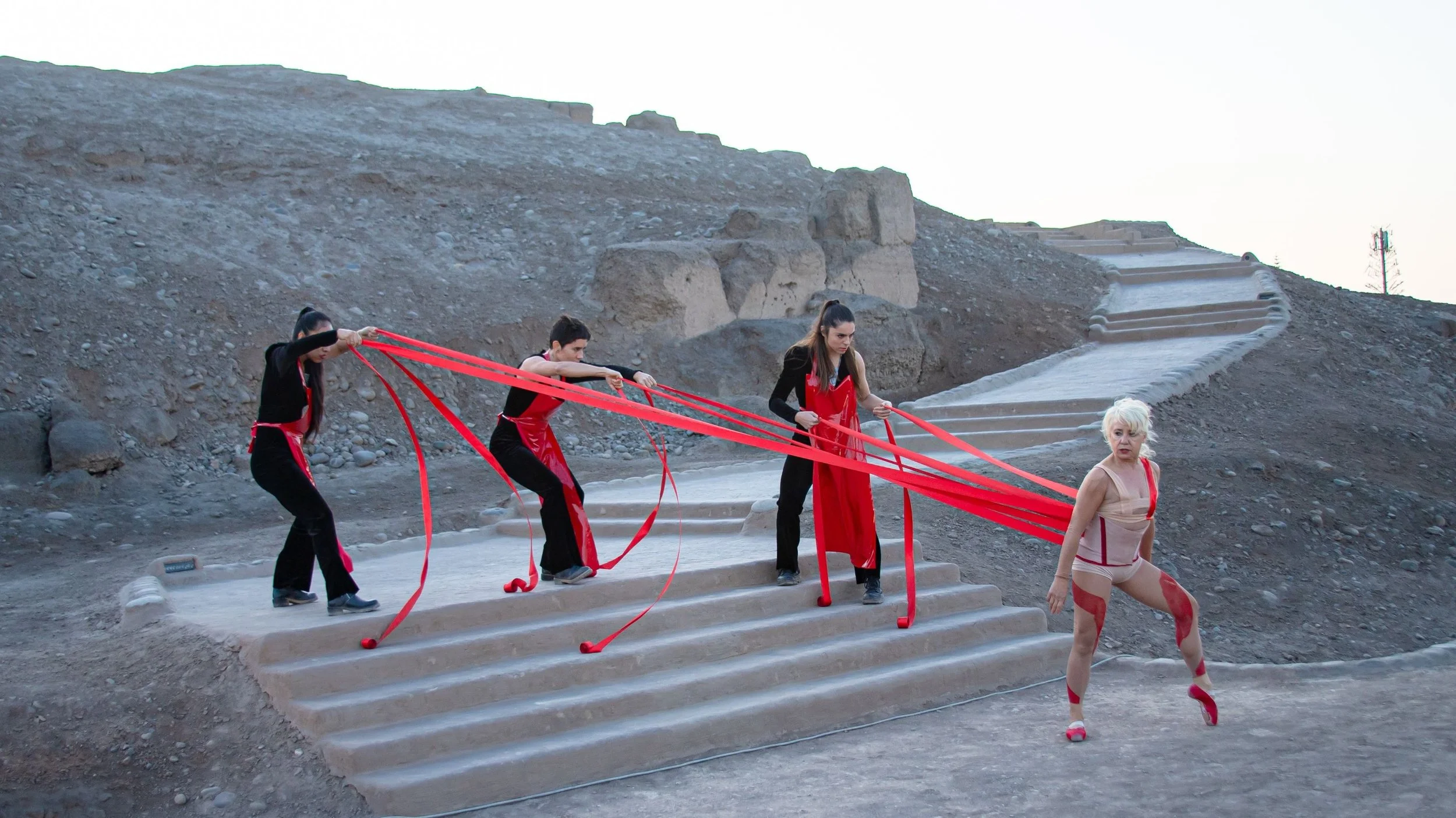 Four female dancers from Sol Pico dance company, three of them connected to one by red ribbons as they perform Lastre (Ballast)