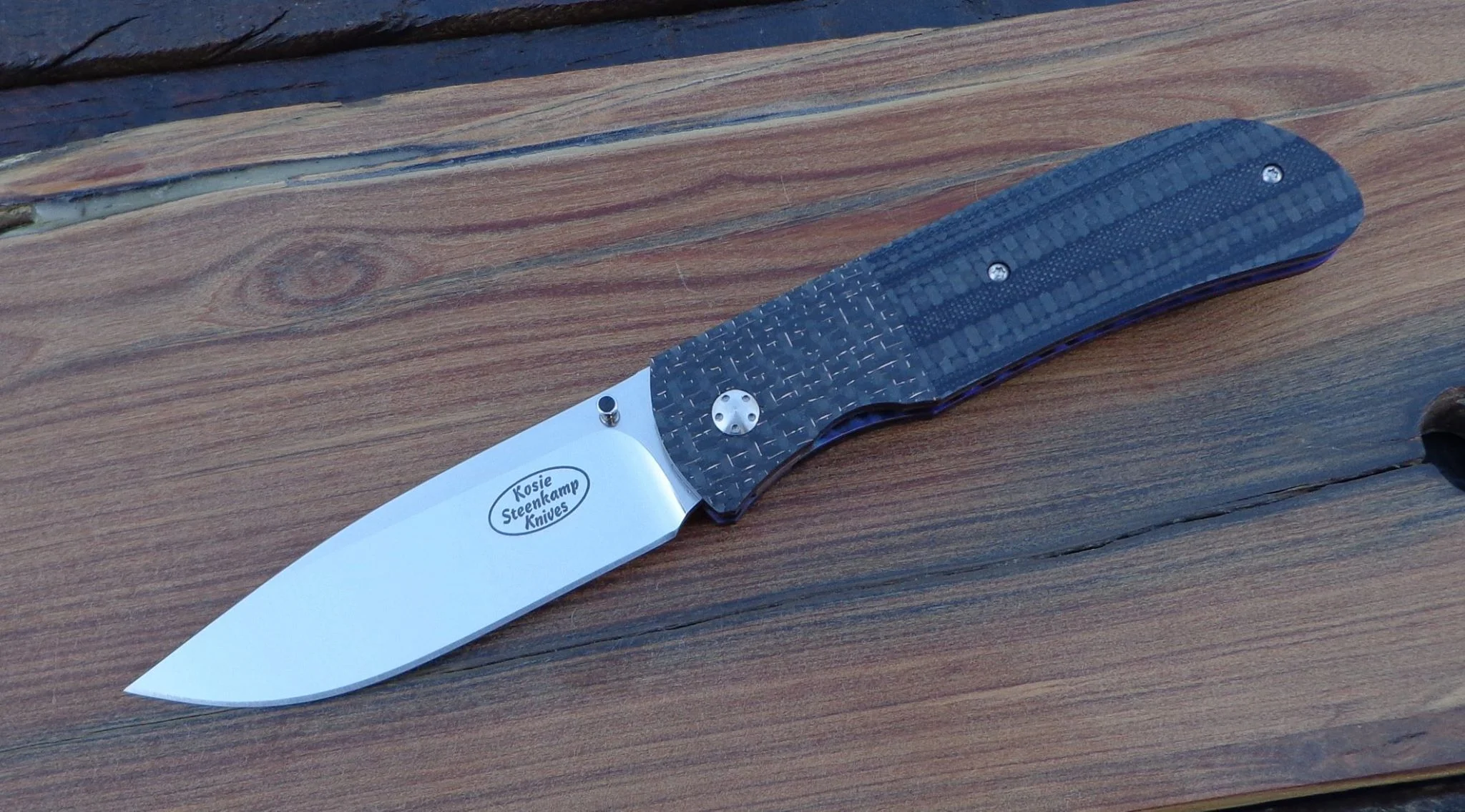 Knife: Hanson. Blade: Böhler N690 Stainless Steel. Liners: Titanium, anodized blue. Handle scales: G10 + Carbon Fibre and Lightning Strike Carbon Fibre with anodized Titanium belt clip.