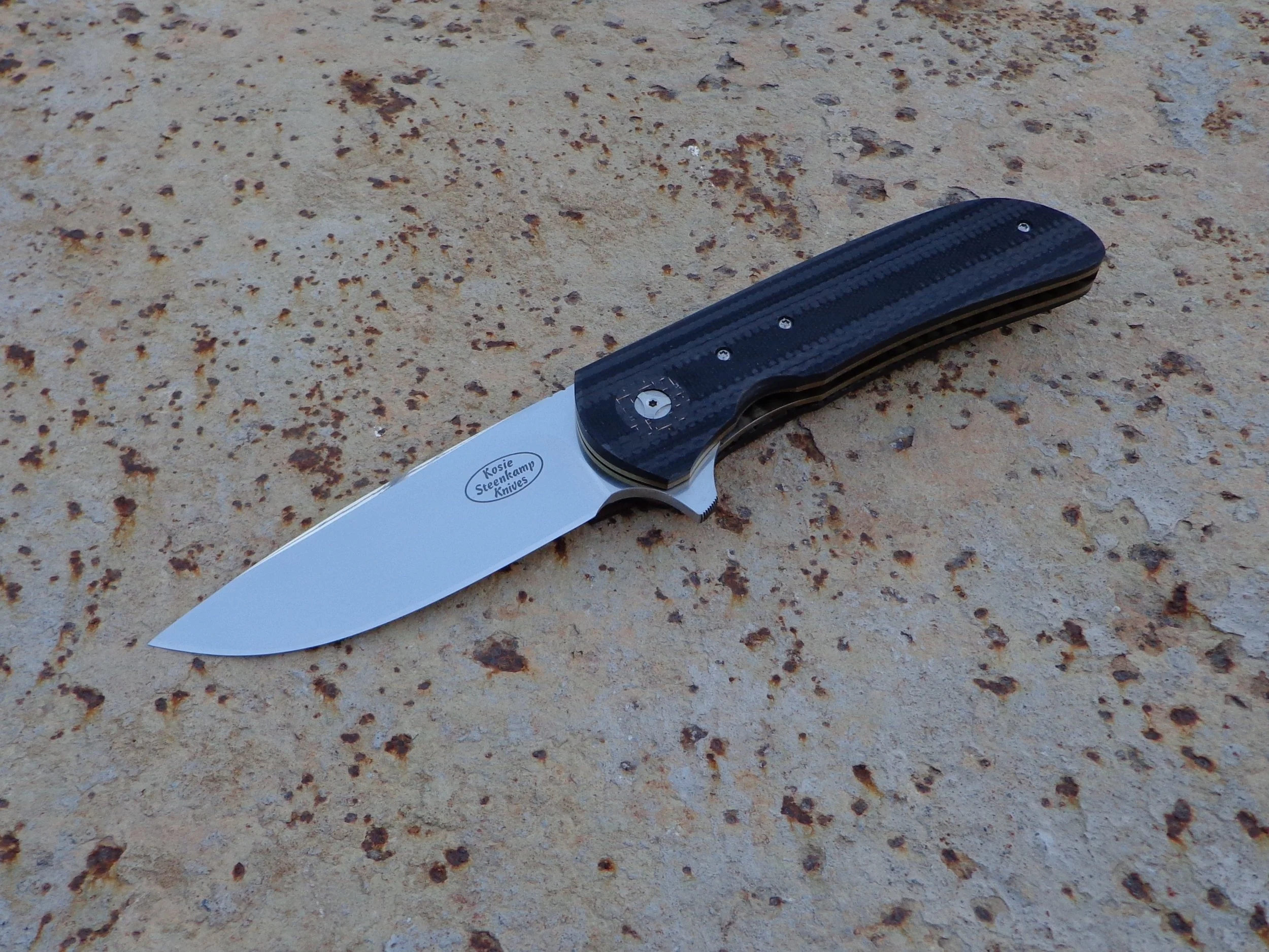 Knife: Piuma Flipper. Blade: Böhler N690 Stainless Steel. Handle scales: Carbon Fiber + G10. Liners and pocket clip: Titanium, anodized golden.