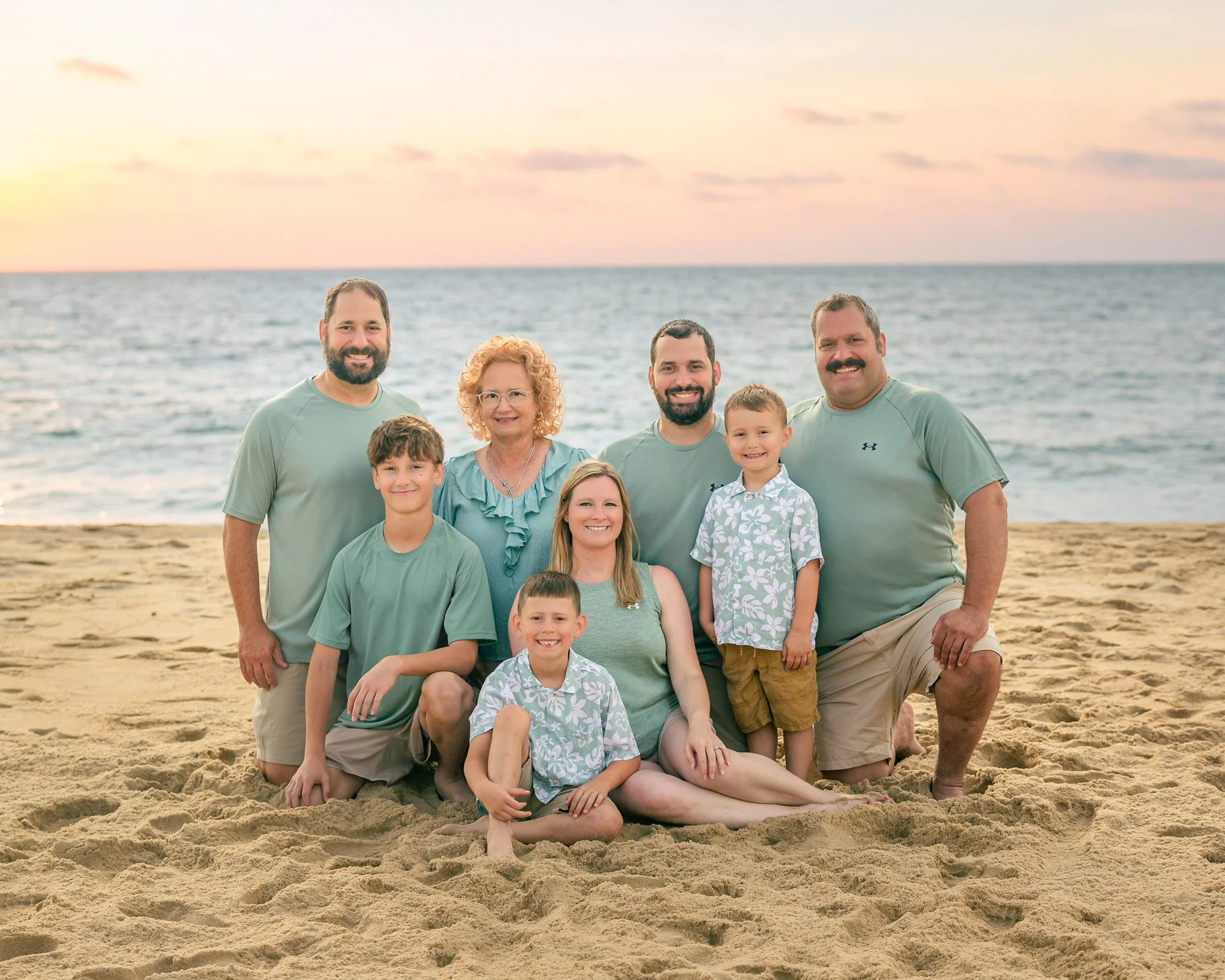 Family group at the beach during sunset, posing for a photo on the sand with ocean in the background.