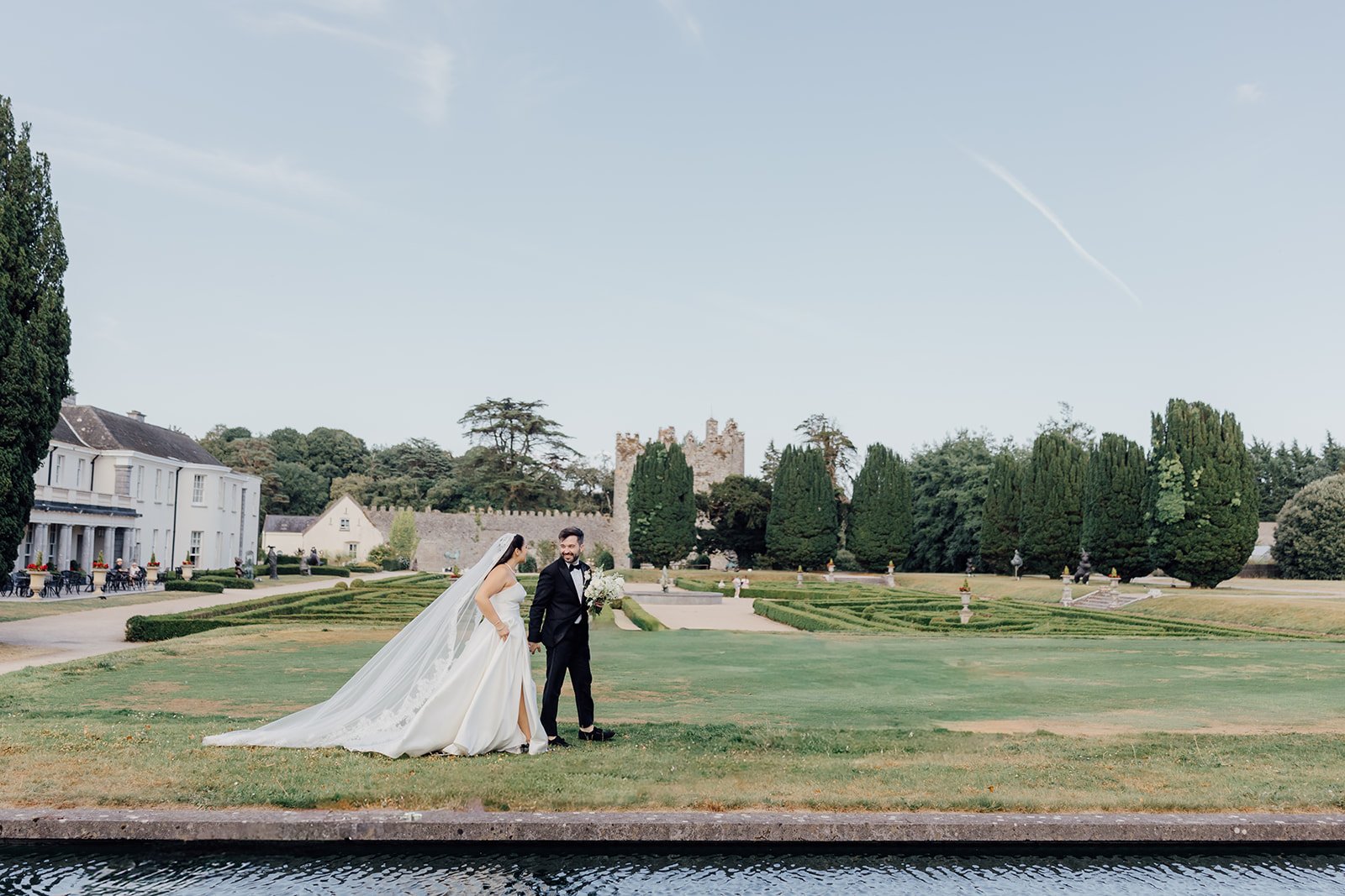 Bride and groom on the lawn with the castle ruins in the distance at Castlemartyr Resort