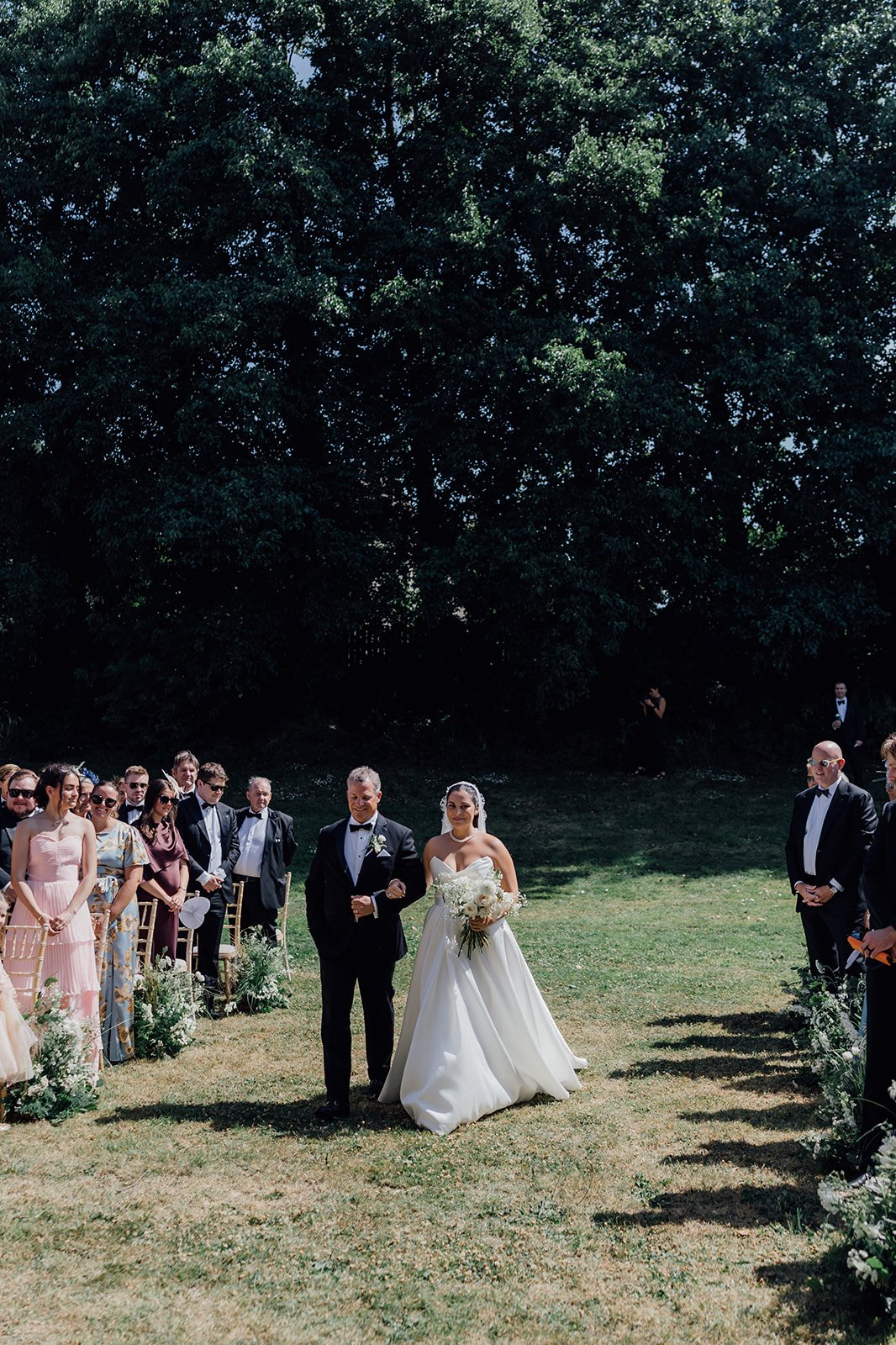 Bride walking down the aisle with her father as guests stand at Castlemartyr Castle