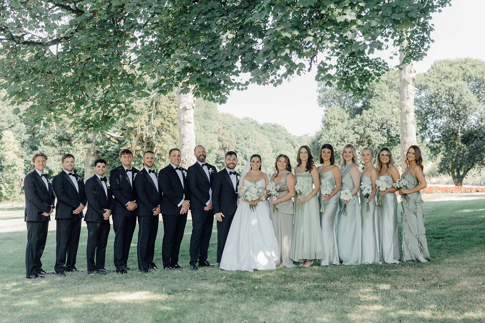 Full wedding party on the lawn at Castlemartyr Resort, groomsmen in black tie and bridesmaids in sage green