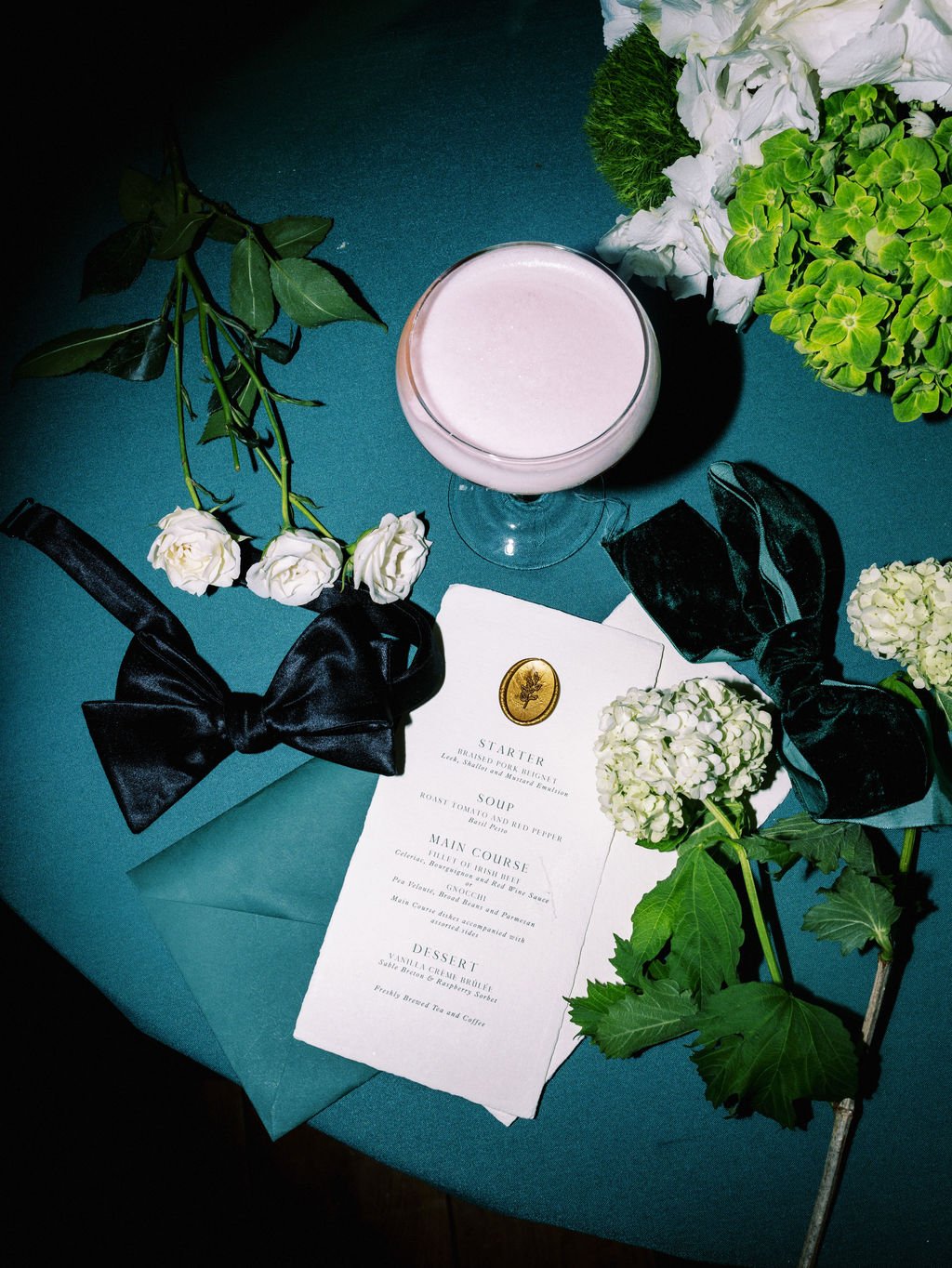 Forest green wedding place setting with menu, black velvet bow and blush cocktail at Sheen Falls Lodge, Kenmare