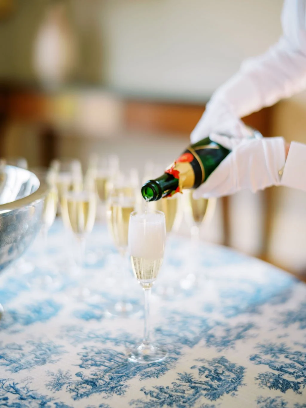 Person in white gloves pouring champagne into a flute at a celebration or event.
