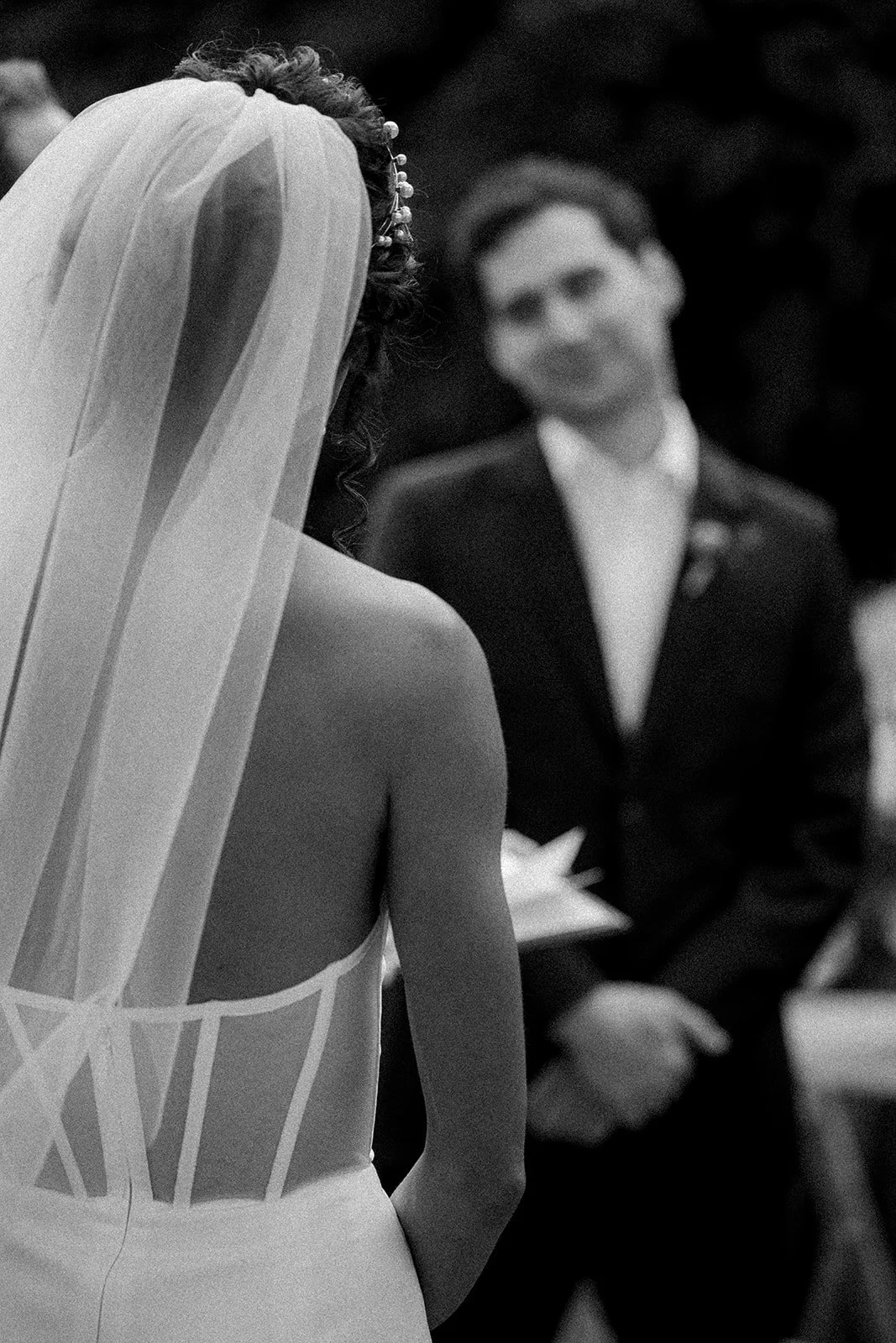 A bride in a wedding dress and veil facing a groom in a tuxedo during a wedding ceremony.