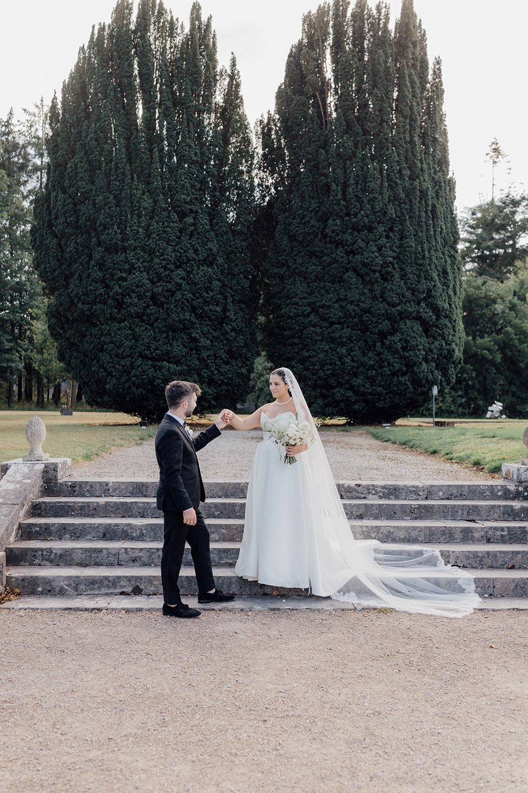 Bride and groom holding hands on the stone steps among the yew trees at Castlemartyr
