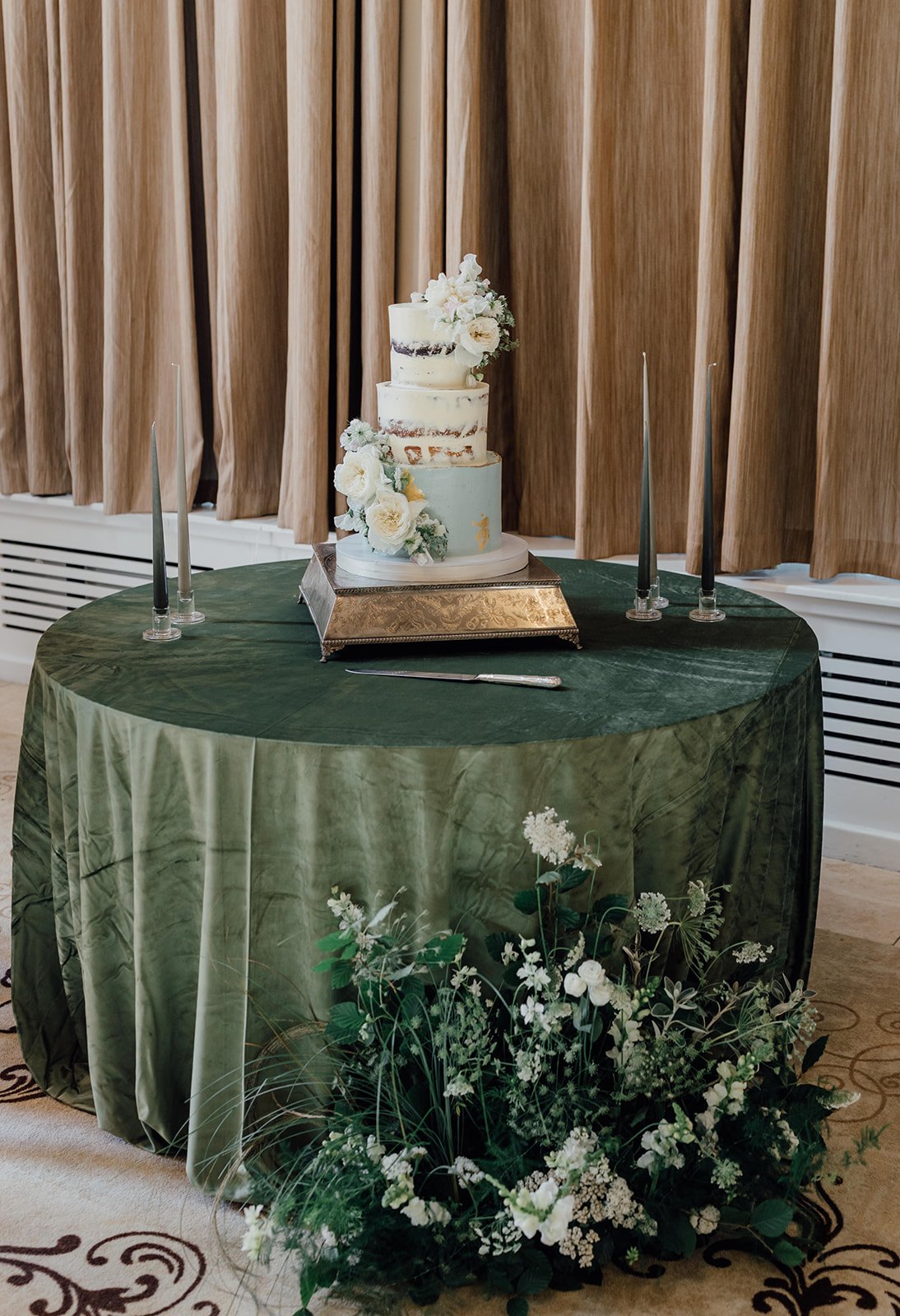 Three tier wedding cake with fresh florals on a green velvet table