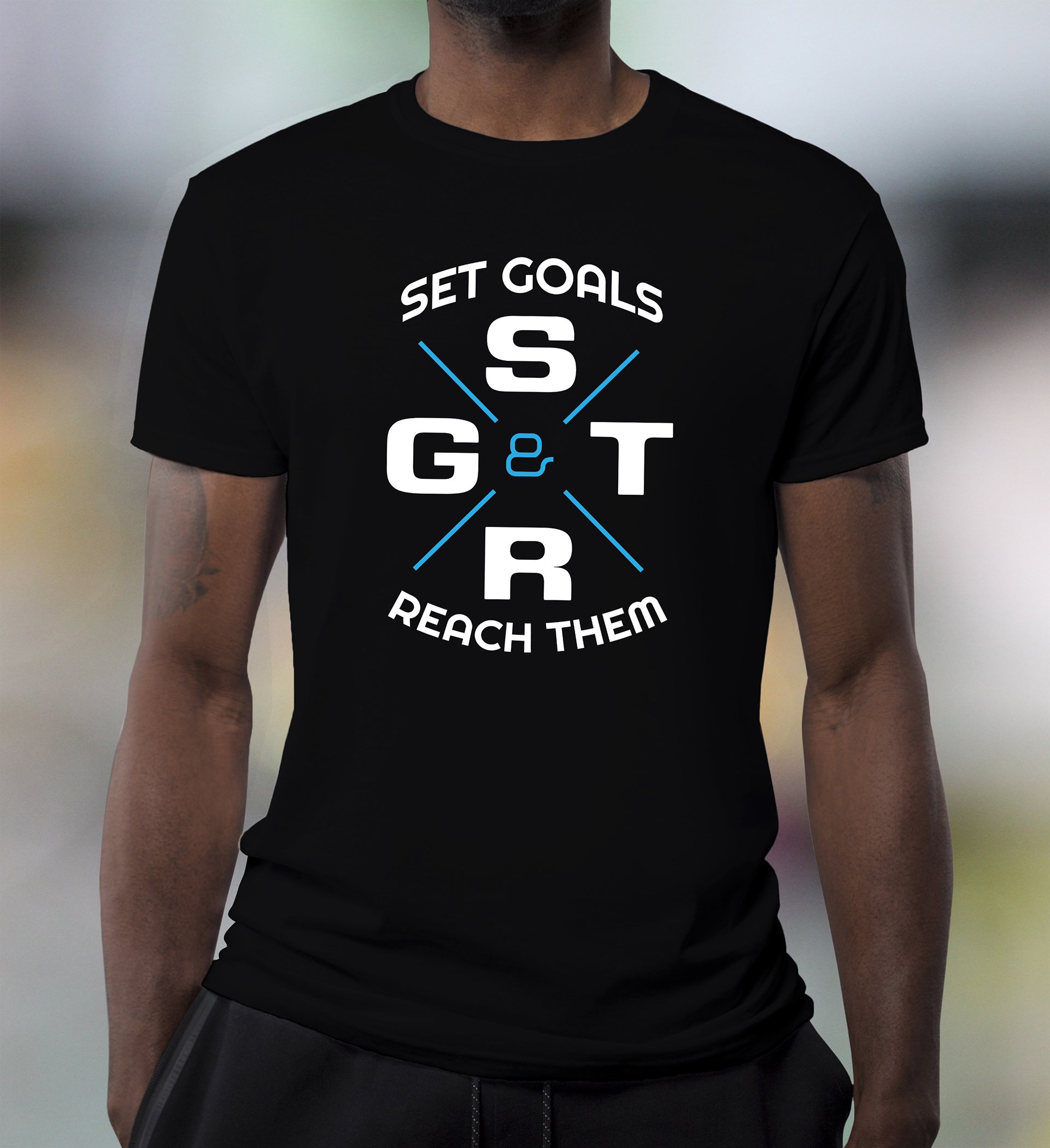 A person wearing a black T-shirt with a motivational quote about setting goals and reaching them, with the words "Set Goals & Reach Them" and the acronym "S G & T R" in a circular design.