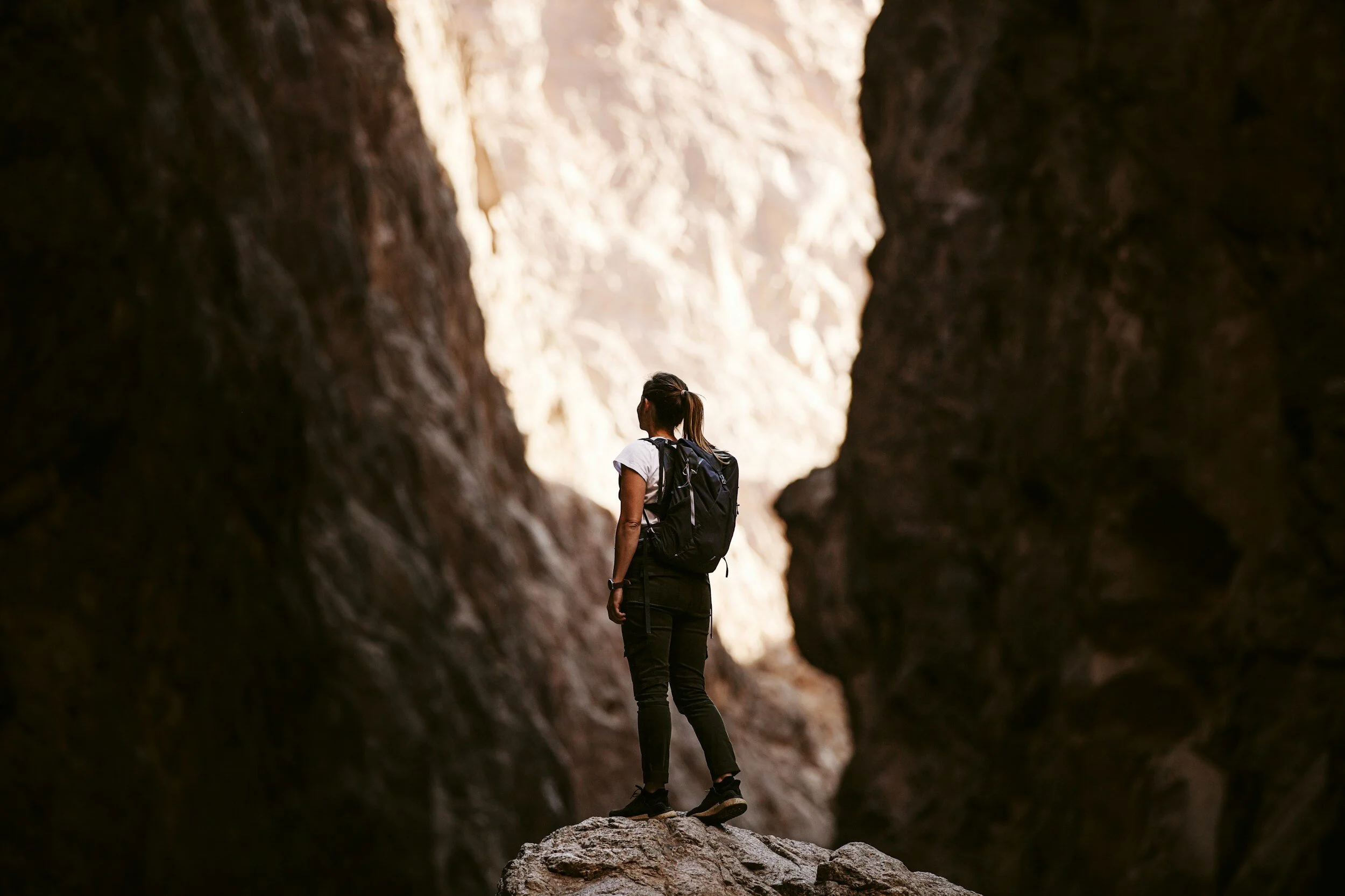 A woman with a backpack hiking through a slot canyon