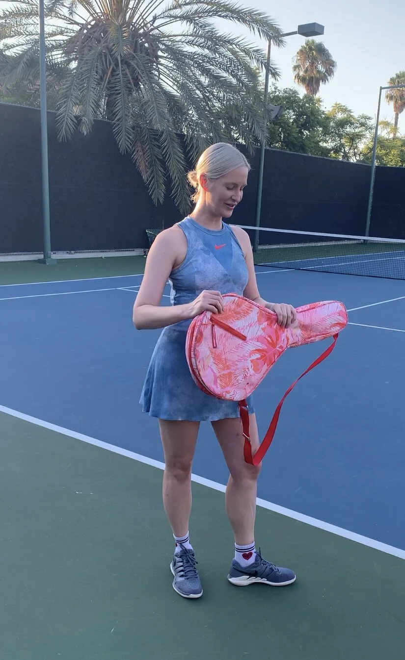 woman on tennis court with decekat tennis bag in tropical print with pink coral red and orange design