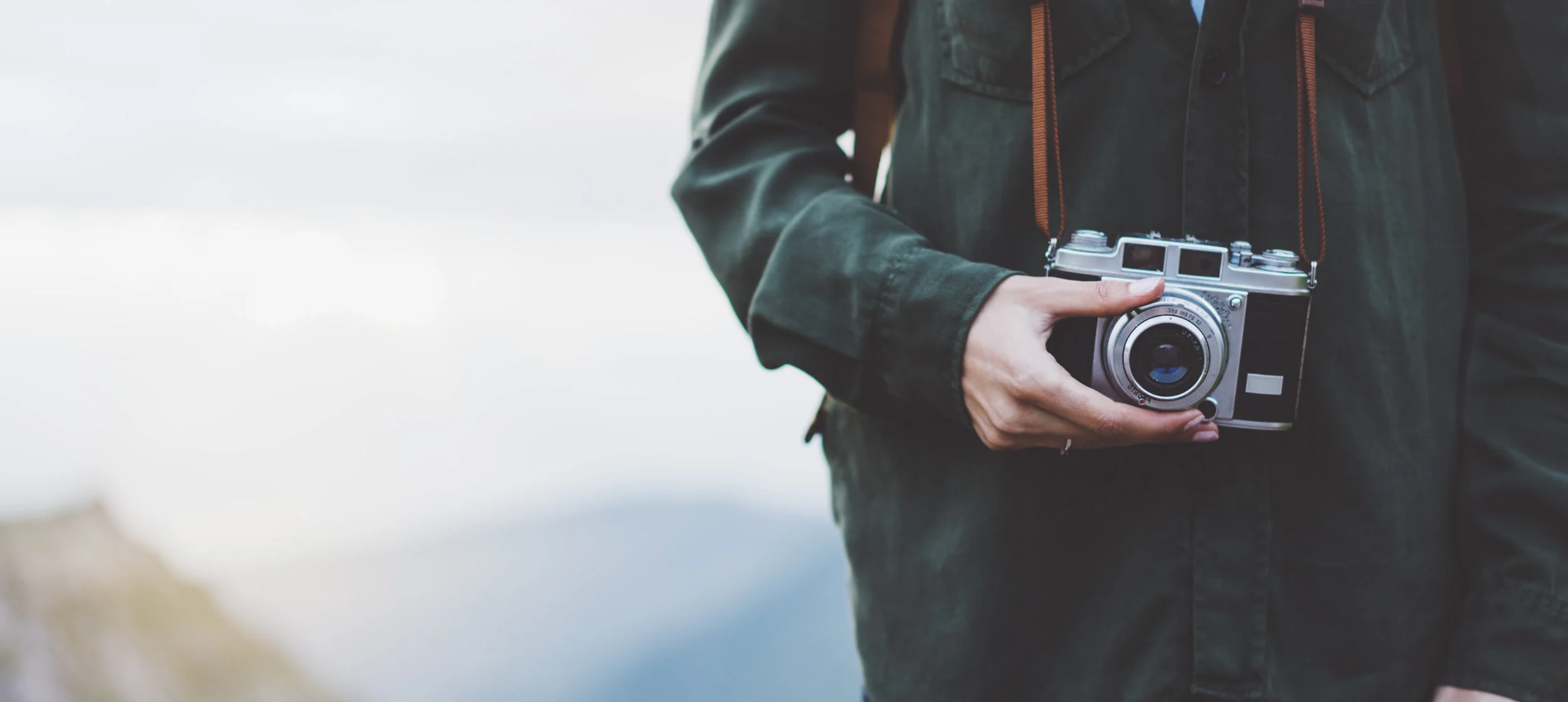 Hipster girl with backpack on peak of foggy mountain, tourist traveler photographer taking pictures of amazing landscape on vintage photo camera on background valley view mockup sun flare