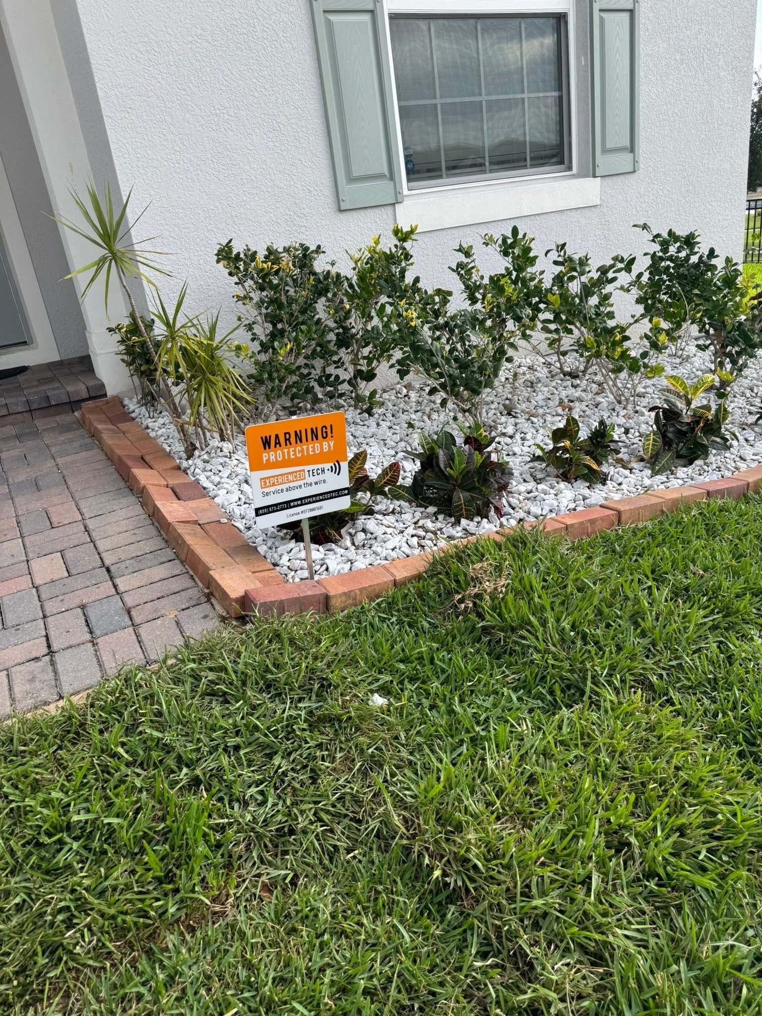 Experienced Tech security yard sign in a landscaped garden outside a home.