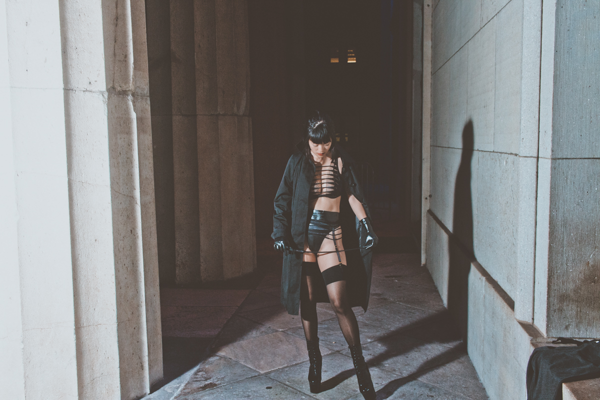 Chinese-American Dominatrix Niko Flux stands in Wall Street in front of the Stock Exchange Building.
