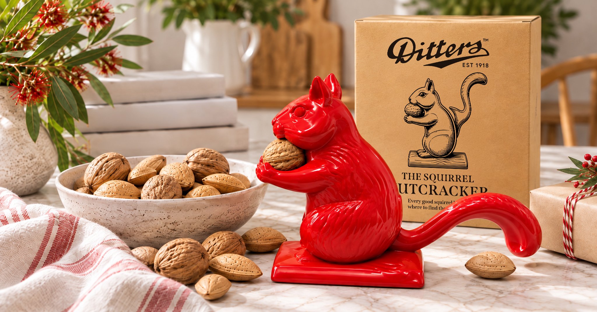 Red Ditters Squirrel Nutcracker beside a bowl of almonds in shell and its illustrated gift box, styled in a warm festive tabletop setting.