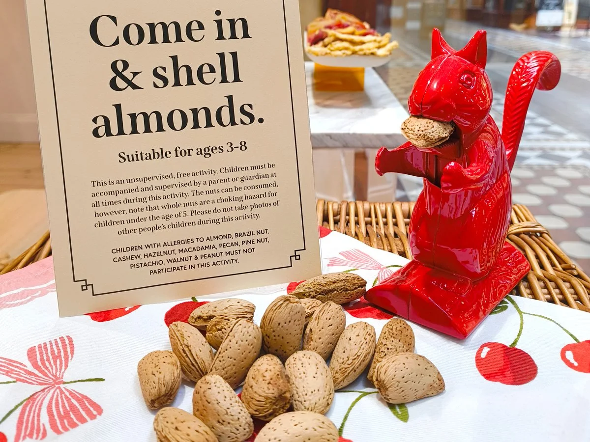 Vintage red squirrel nut cracker beside a bag of raw almonds in shell and cracked almonds on a festive table setting.