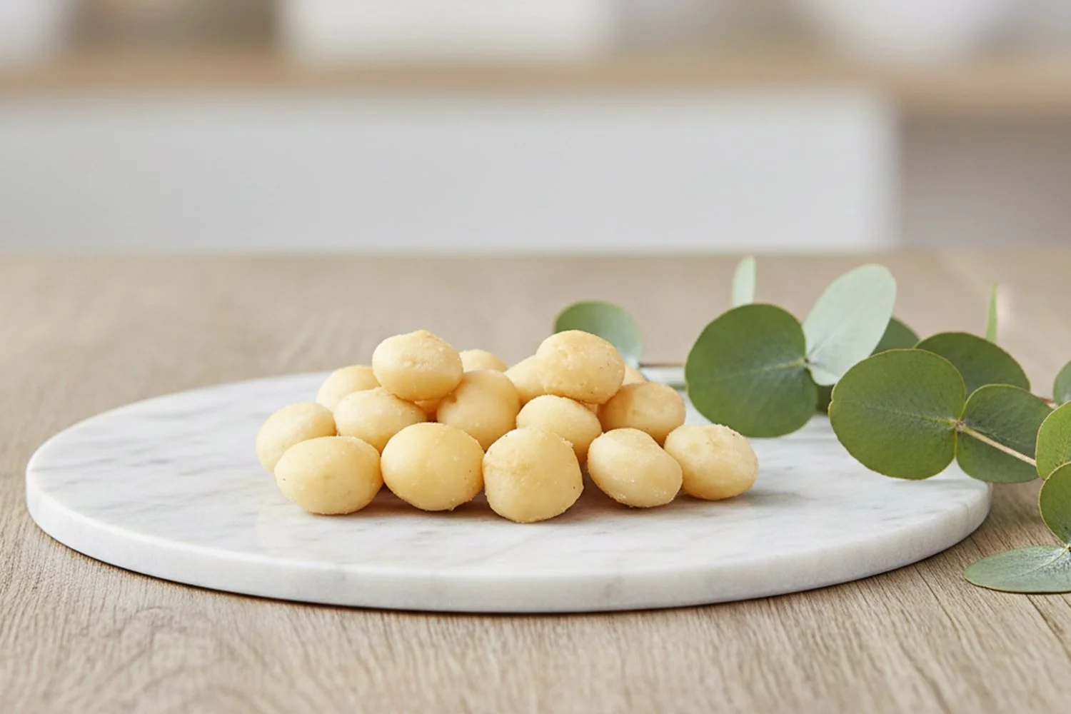 roasted macadamias on marble platter with a sprig of eucalyptus leaves on the side