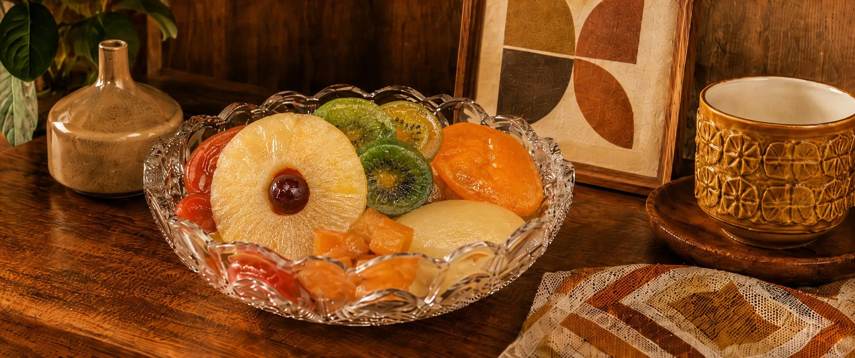 Glacé fruit arranged in a crystal bowl on a warm retro-style table beside a ceramic cup.