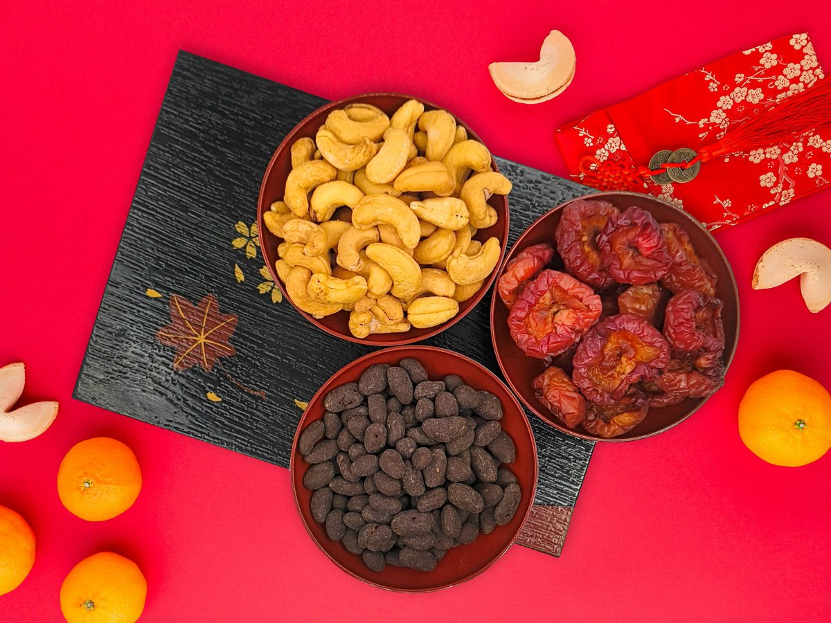 Ditters salted cashews, dark chocolate goji berries and australian dried plums in red lacquer bowls next to oranges and fortune cookies