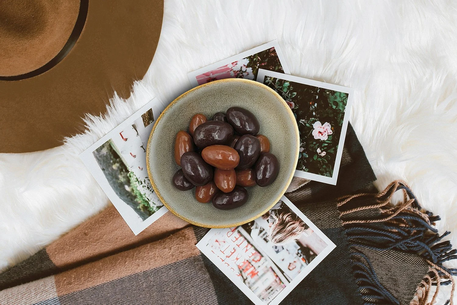 milk and dark scorched almonds in a stone bowl next to some polaroid photos, a hat and a brown checked scarf