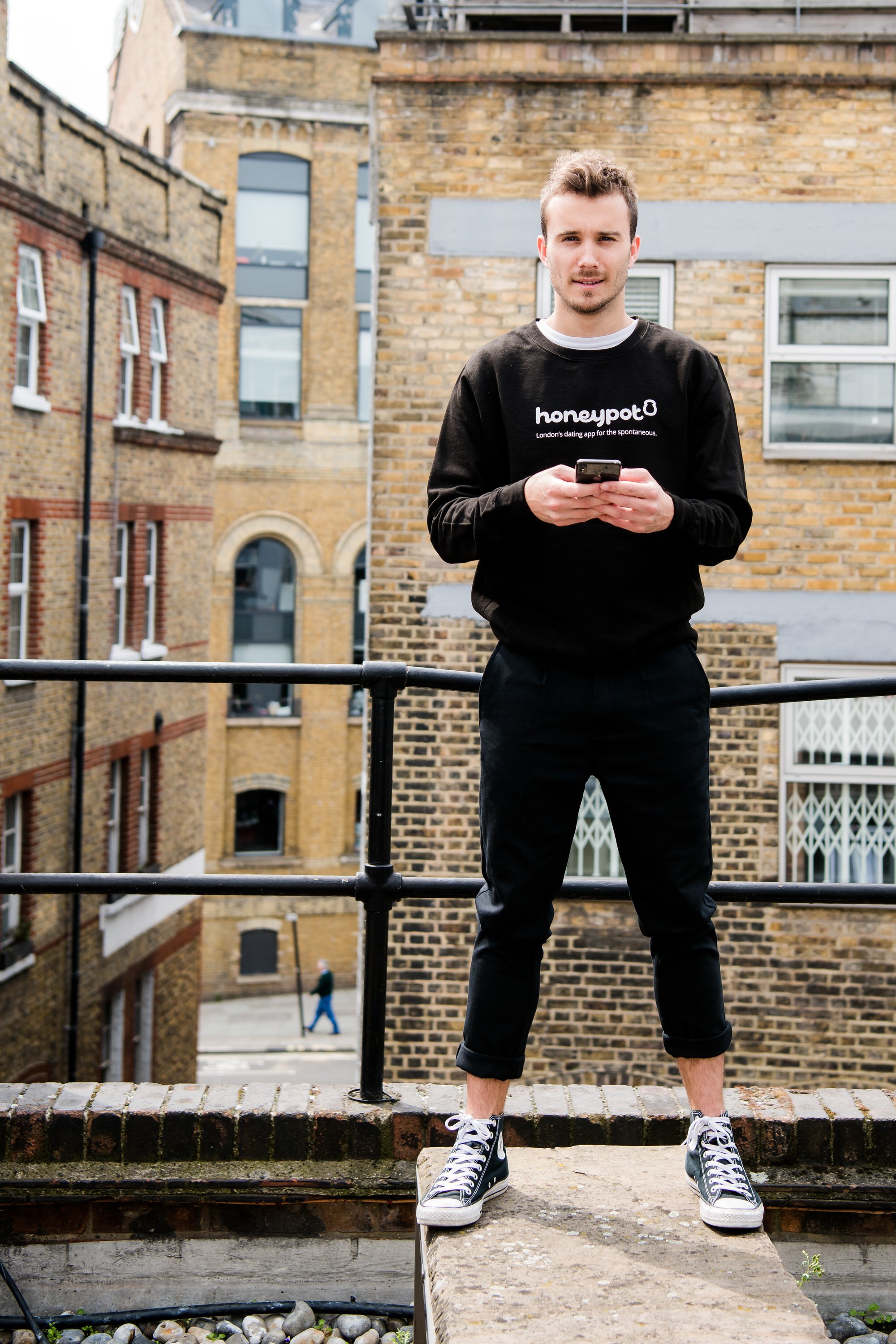  Young man on phone and branded black tracksuit standing on top of a city building. 