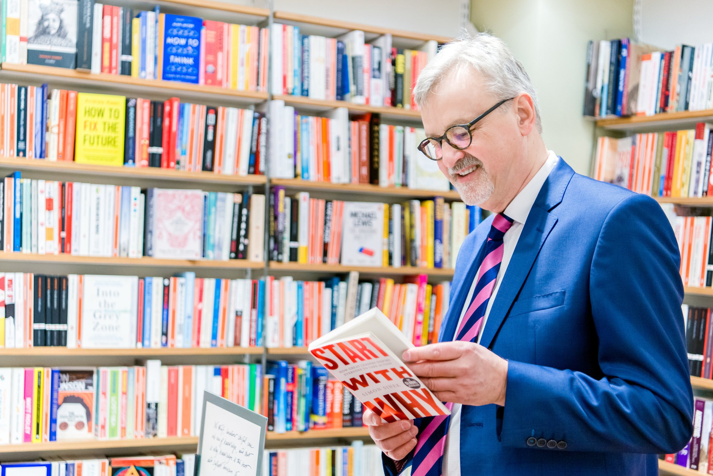  Man in suit holds up business book against a colourful background in a book shop 