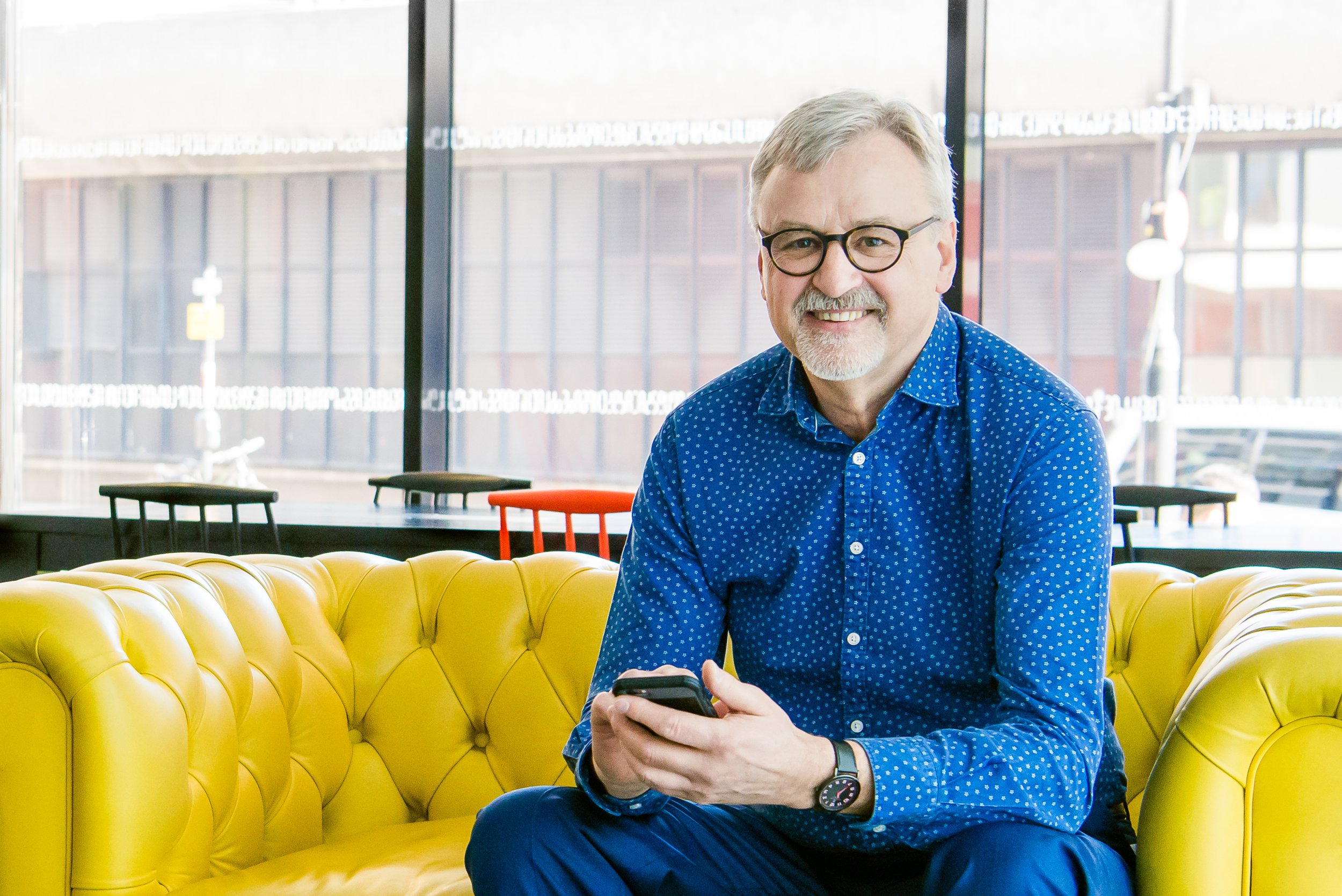  Business owner sits on a bright yellow sofa, looking into the camera 