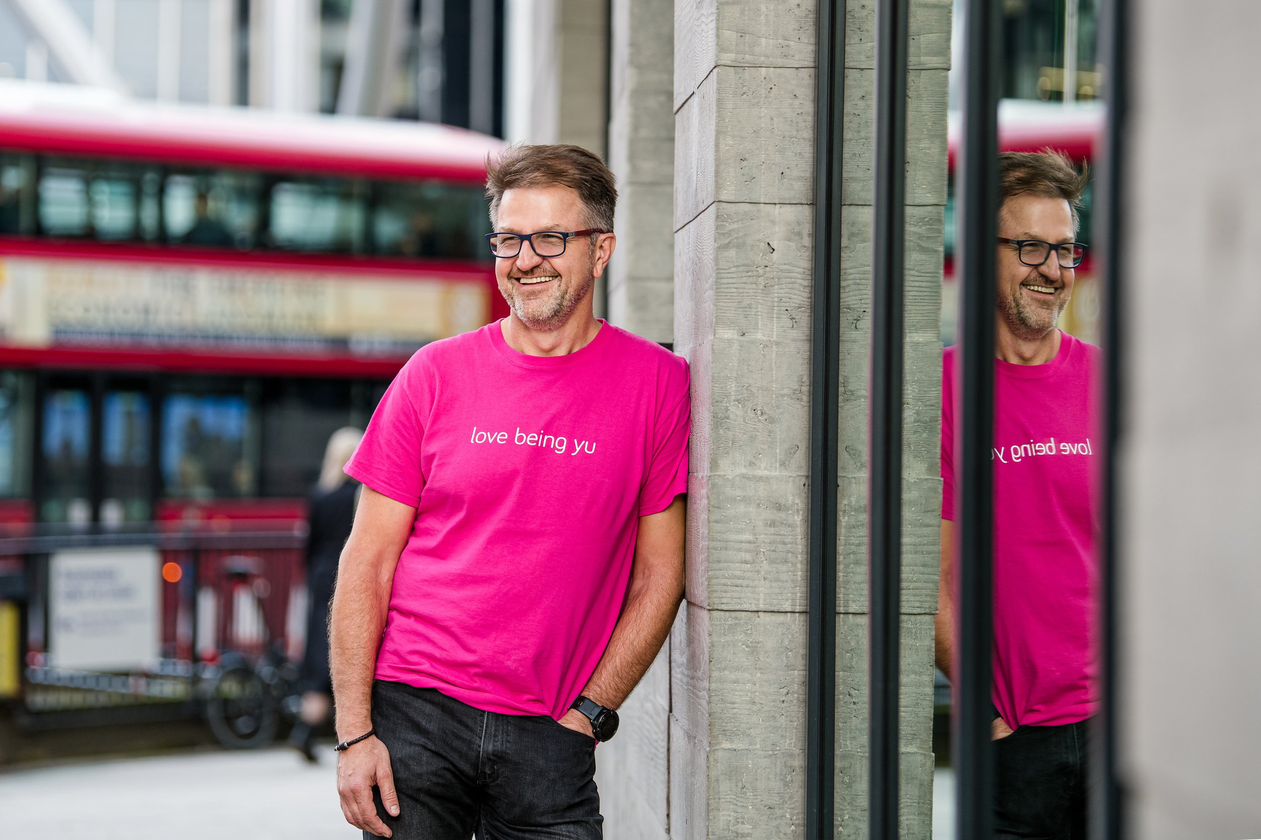  Business man in branded pink t-shirt poses outside on London street. 