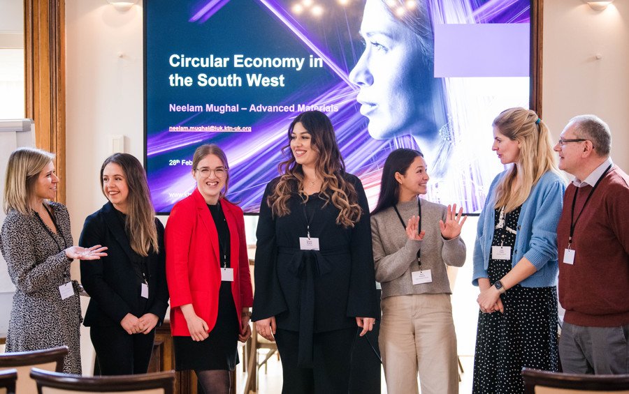 Group photograph at conference with a projector screen behind showing a woman in innovation