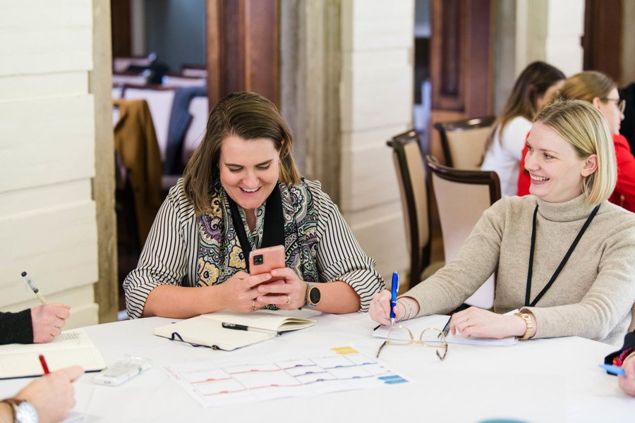 two women wearing lanyards at a table laughing at work event
