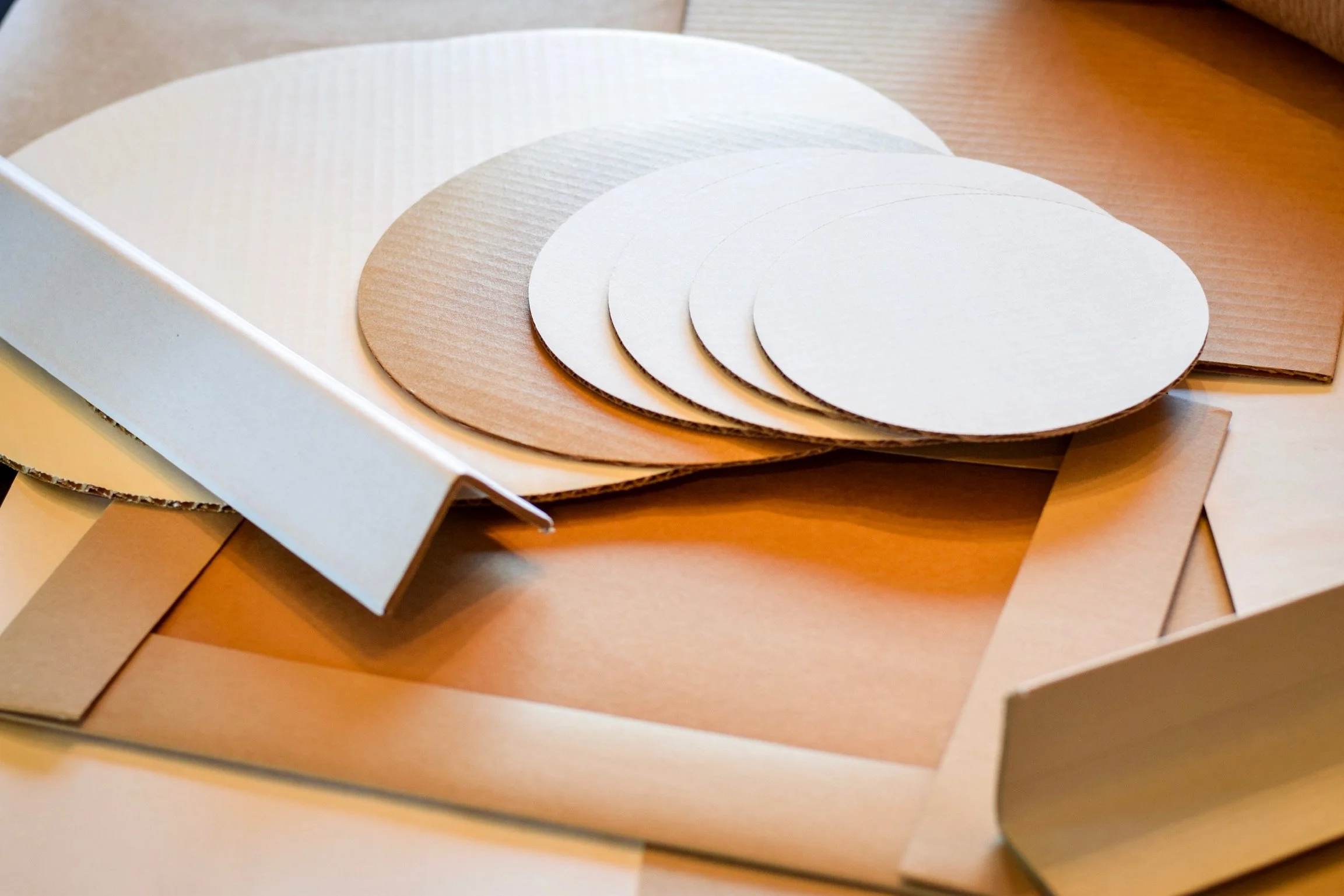 Close-up of several sheets of colored paper in shades of white, beige, and light brown, fanned out on a wooden surface.
