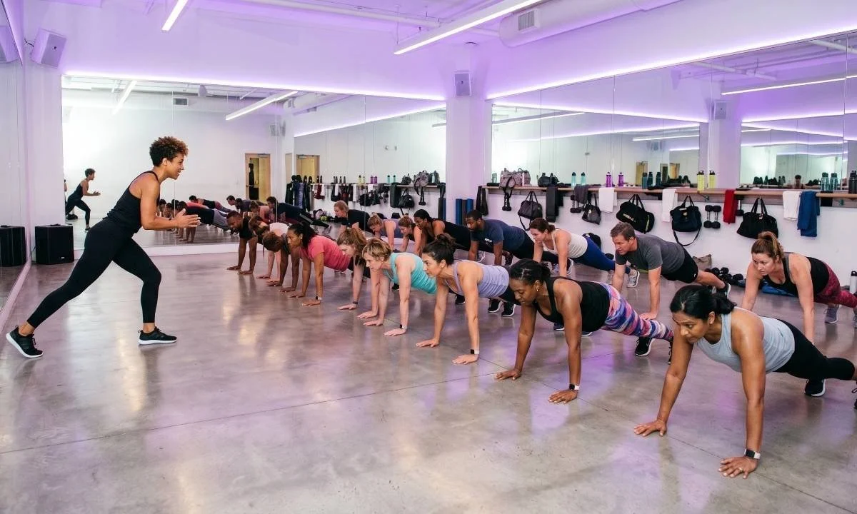 A diverse group fitness class performing a HIIT workout together in a modern fitness studio.