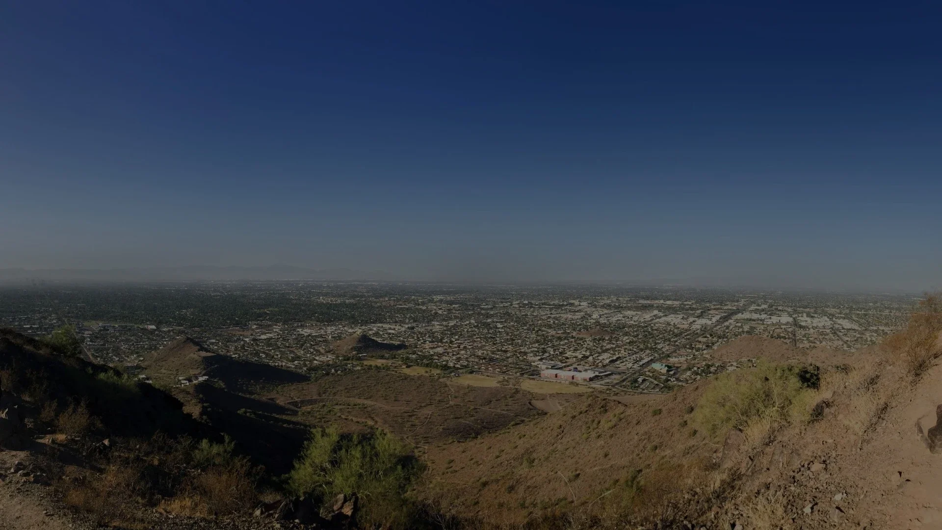 Panoramic view of Peoria with desert hills in the foreground and sprawling city neighborhoods extending toward distant mountains.webp