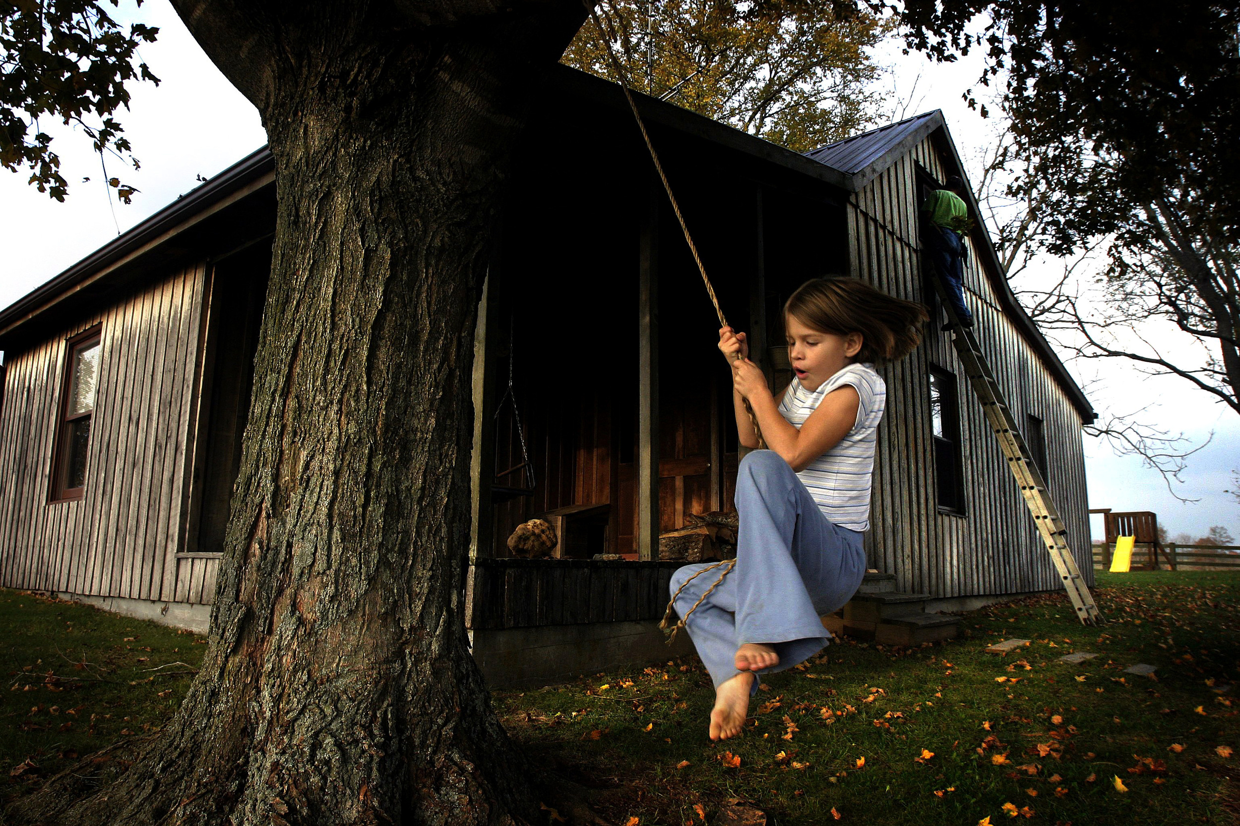  Anna Stewart Burdette, 7, swings on a rope swing in the front yard while her father paints an upstairs window of their house. The Burdettes were given an abandoned two room board and battan house which they refurbished in Marion County. 