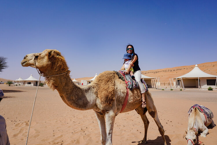 Mom-smiling-with-baby-on-camel-ride-in-camp-Desert-Nights-Camp-Oman-Wahiba-Sharqiya-Sands.jpg