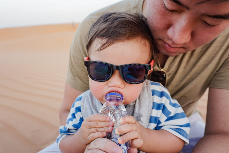 Baby-wearing-sunglasses-drinking-water-bottler-desert-dunes-with-dad.jpg