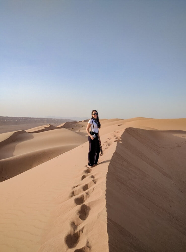 Woman-walking-with-camera-top-sweeping-desert-dunes-Oman-Wahiba-Sharqiya-Sands.jpg