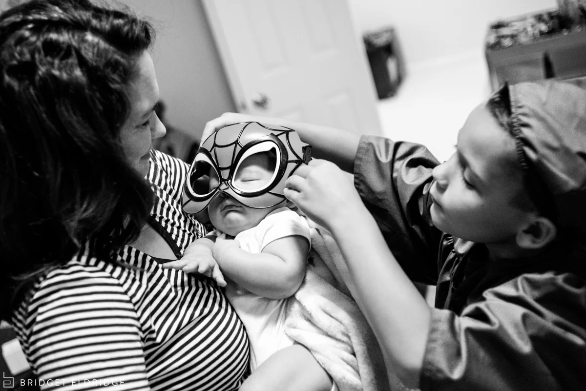 big brother dresses up his three month old brother with a spiderman mask