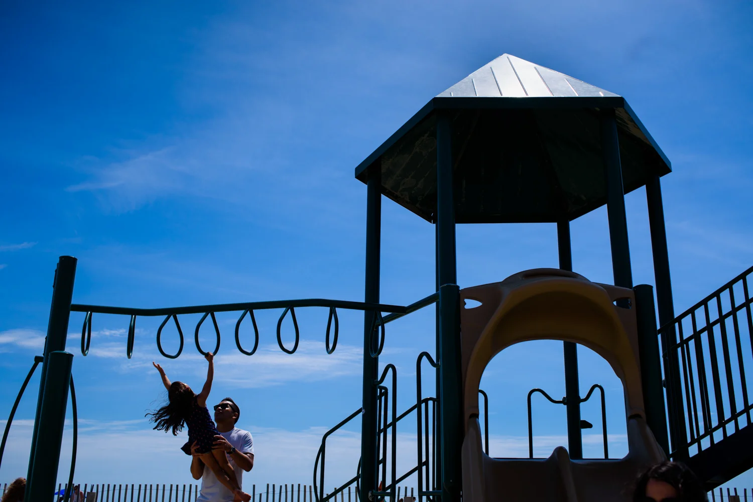dad helps his daughter go across the monkey bars