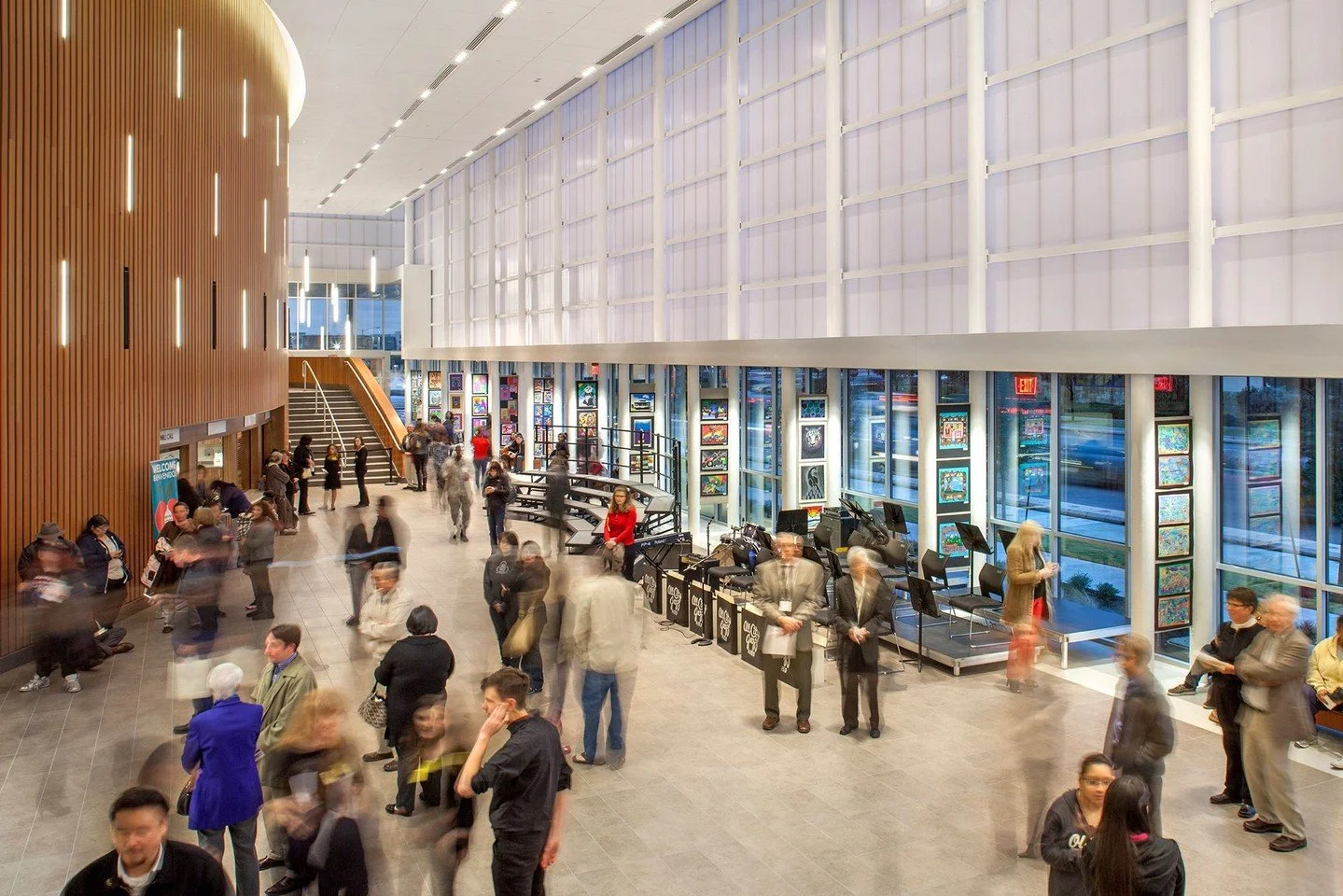Visitors to the Performing Arts Center enter a spacious lobby. The horizontal plane of the trellis outside continues into this space, defining a narrow gallery consisting of panels with rotating exhibitions of student artwork. #AISDPerformingArtsCent