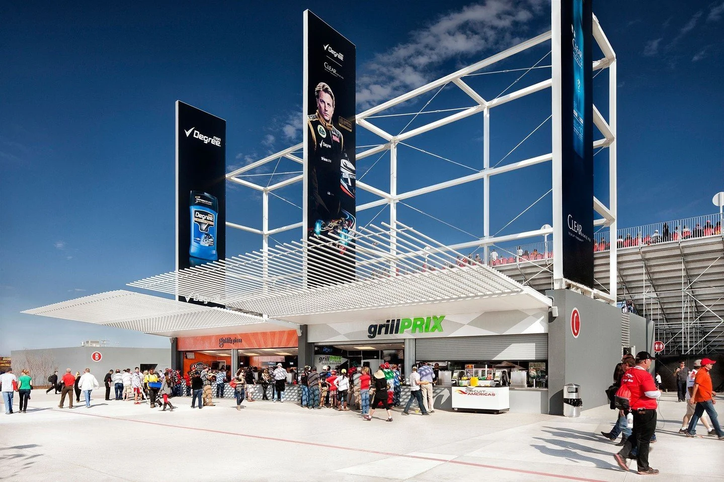Large banners and bold graphics punctuate a trellis-covered pedestrian promenade along the Grand Plaza's northeast edge, with amenities including concession stands, retail areas, restrooms, and grandstands. #CircuitofTheAmericas #MiroRiveraArchitects