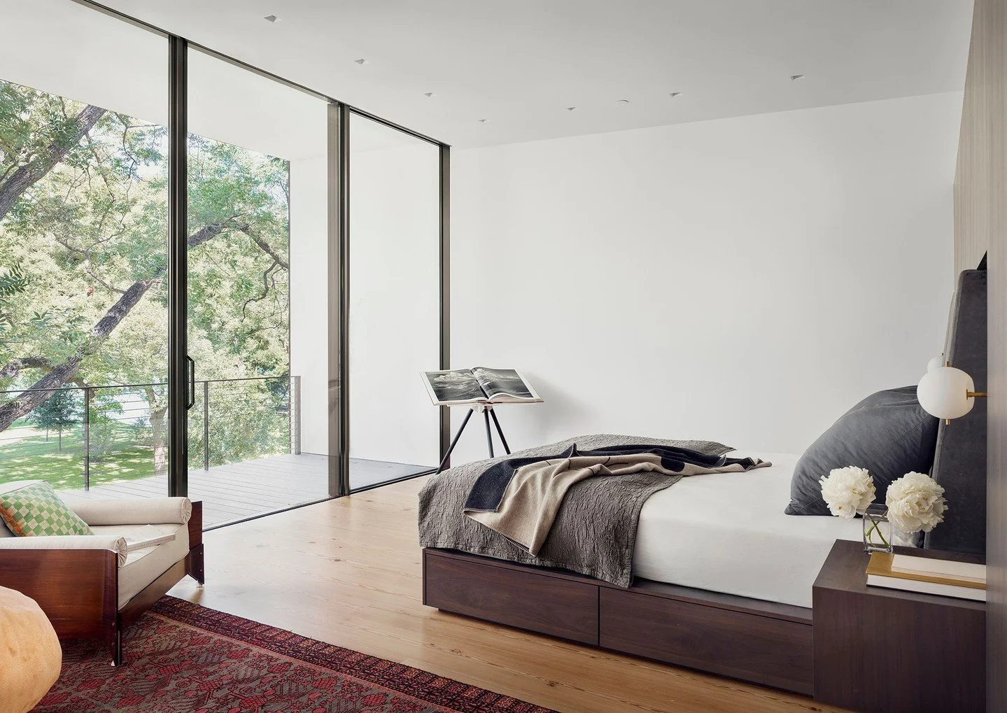 Perched on the southeast corner of the residence, the primary suite embraces a palette of gray leather, rich walnut, and dark basalt. The primary bedroom opens up to a private balcony that feels like a treehouse among the pecan branches. #RiverHillsR