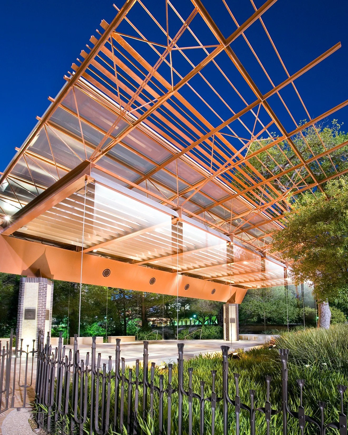 Fans, speakers, and shades are seamlessly integrated to maintain the clear expression of the structure. Overhead, the roof slopes to a central spine, where a sloping gutter cantilevers to channel rainwater so that it falls freely into a catch basin. 
