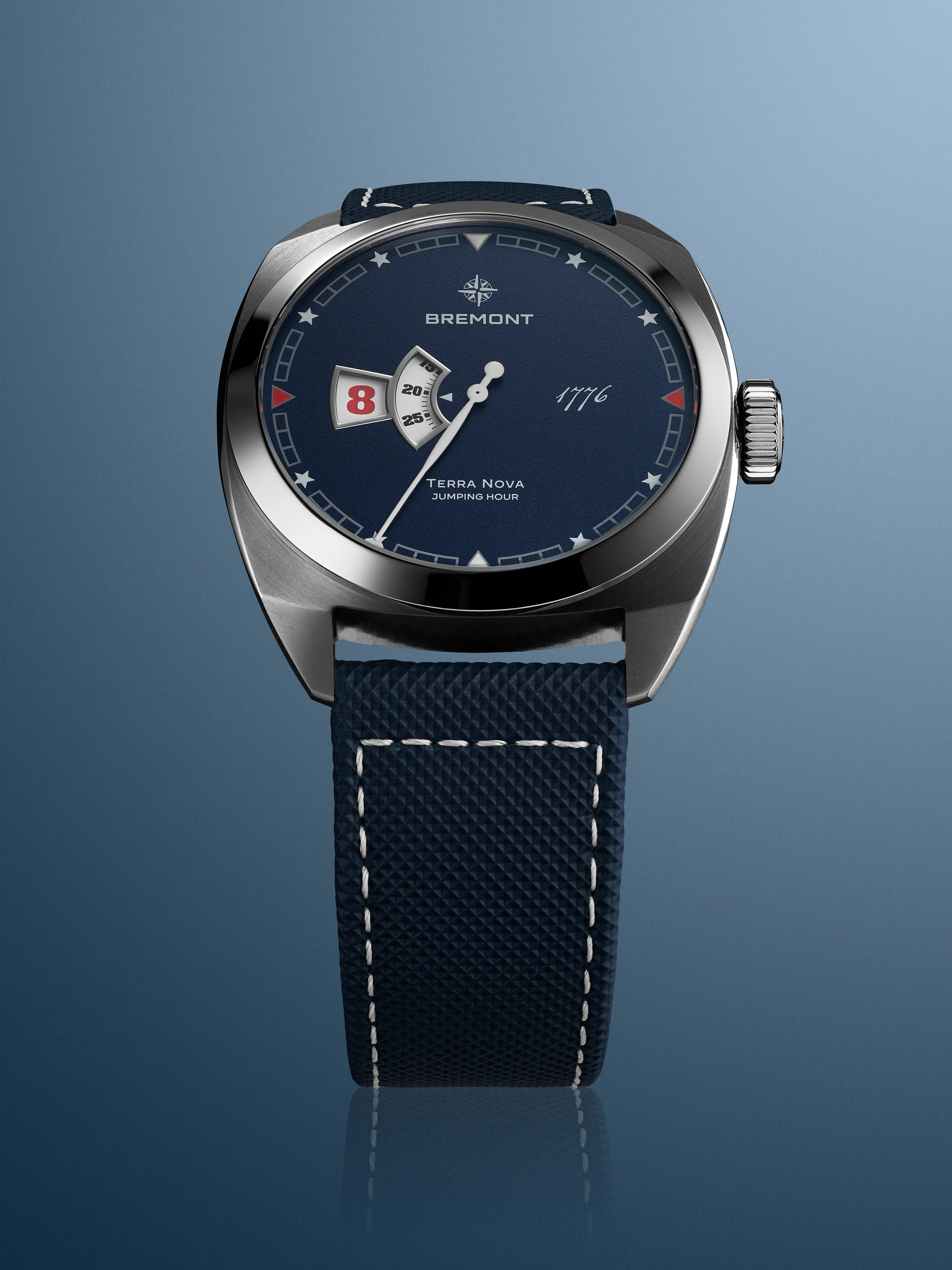 A Bremont Terra Nova Jumping Hour wristwatch with a blue textured strap, dark blue dial, and a digital jumping hour display, set against a blue gradient background.