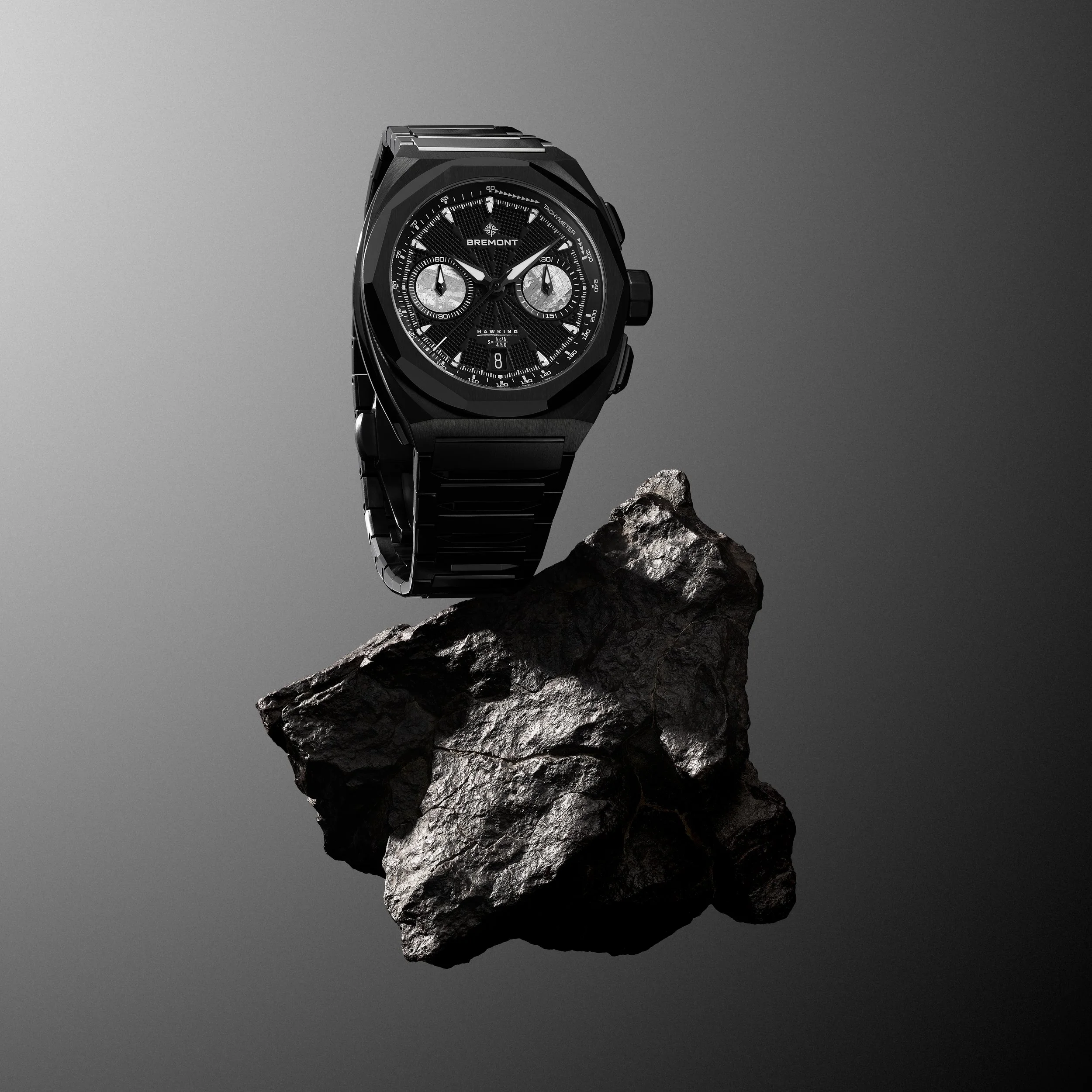 A black Bremont Hawkings wristwatch with a metallic band, displayed on a rugged rock against a neutral gray background.
