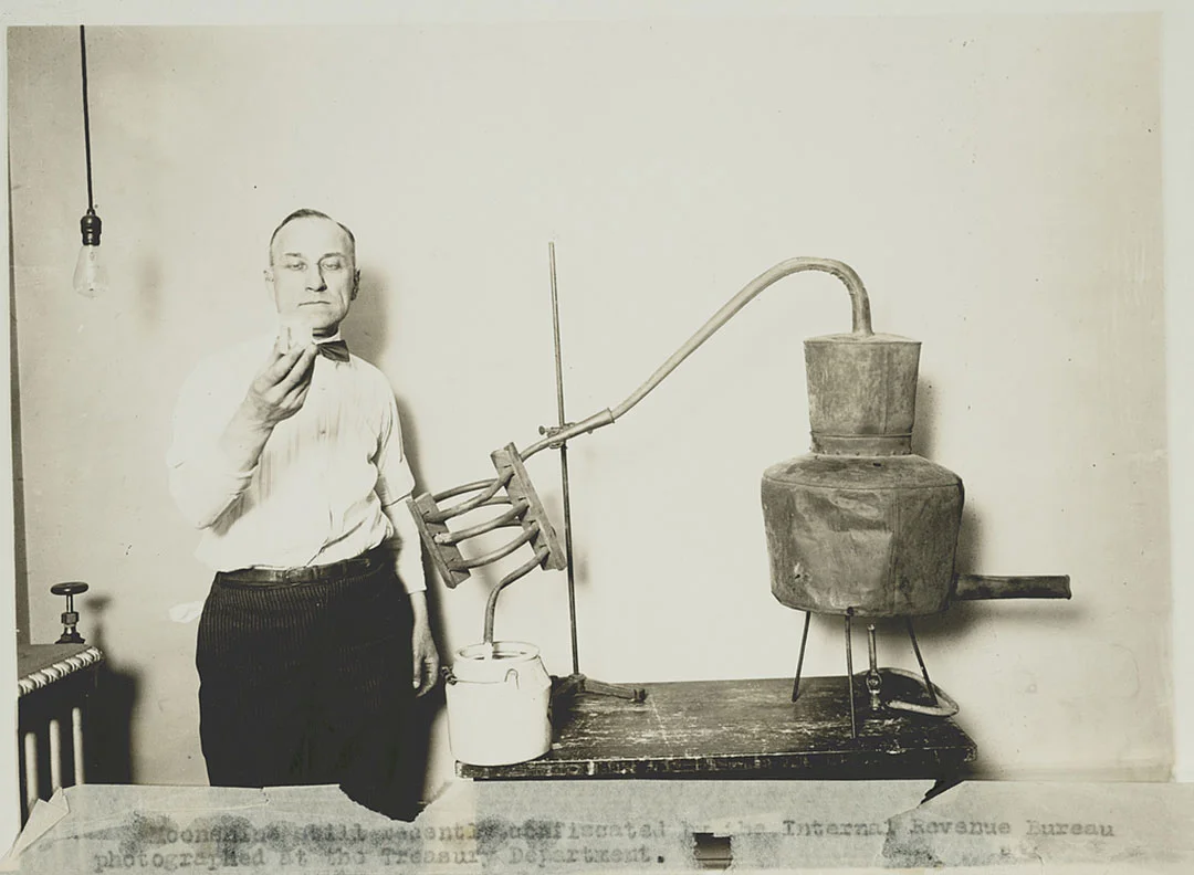 An Internal Revenue Service agent scrutinizes the contents of a moonshine still during the Prohibition era.